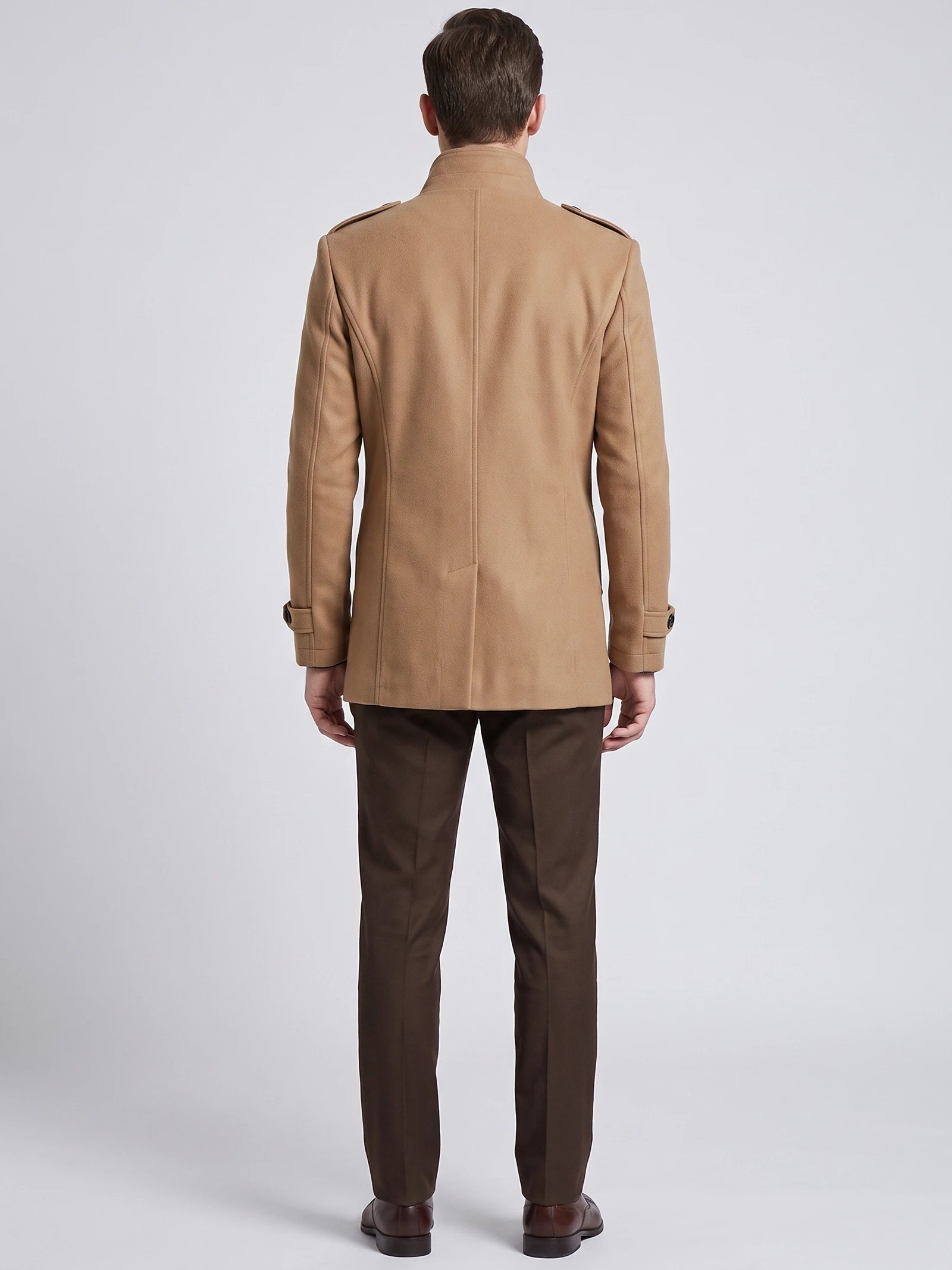 Rear studio view of a model wearing a Khaki wool overcoat with shoulder tabs, back seam detailing, and belted cuffs.