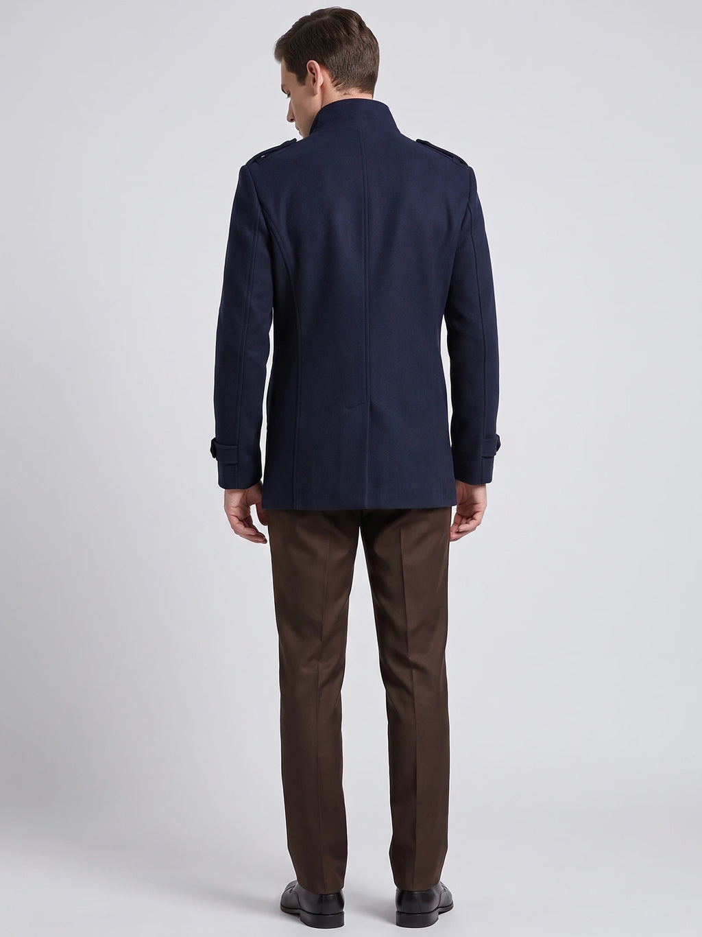 Rear studio view of a model wearing a Navy wool overcoat with a stand collar, shoulder tabs, cuff straps, and a center back seam.