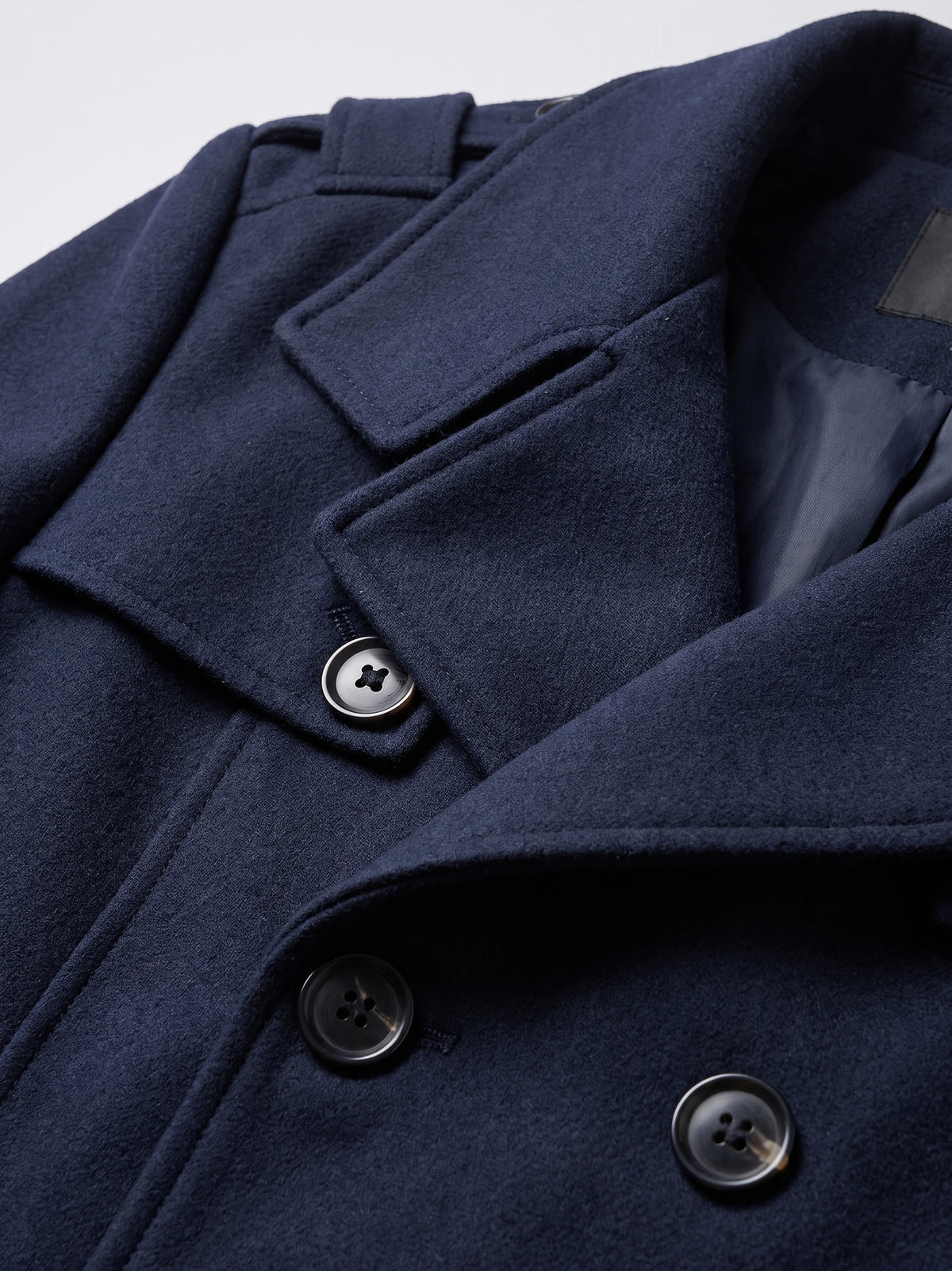 Close-up of a Navy wool men’s overcoat showing the notched lapel, buttoned front, and inner lining.