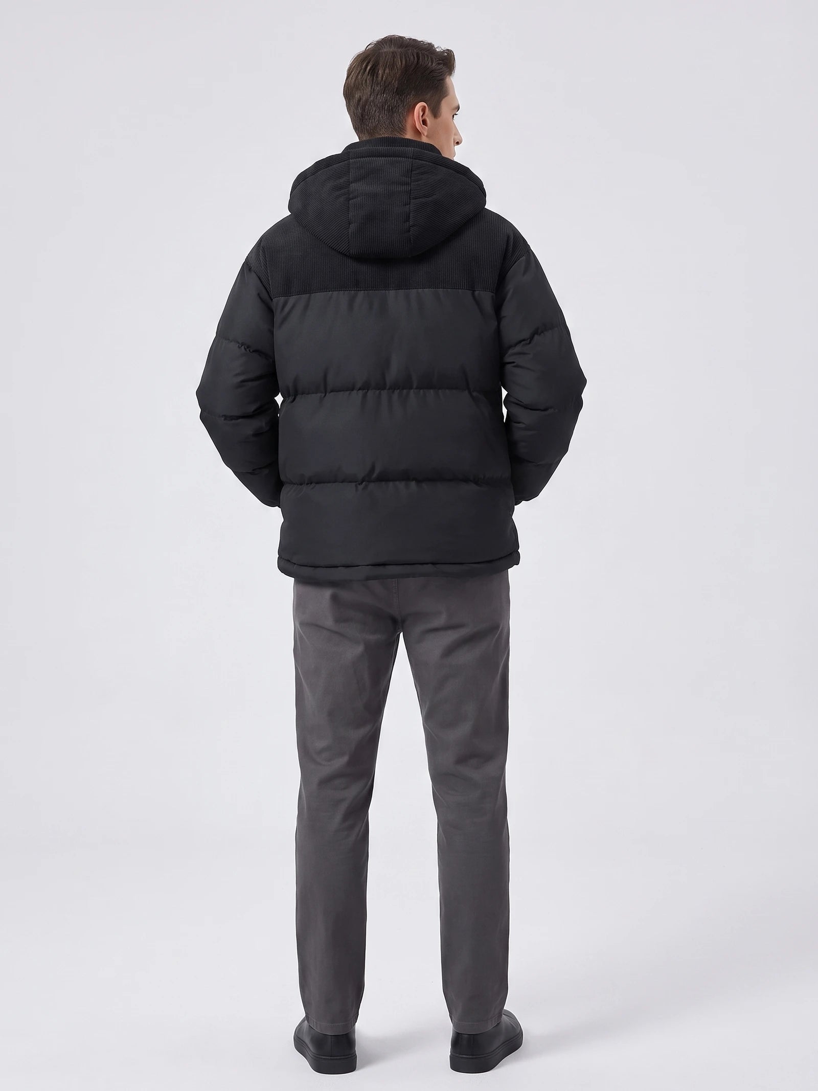 Rear studio view of a model wearing a Black padded puffer jacket with a hood, ribbed upper back panel, and quilted insulation.