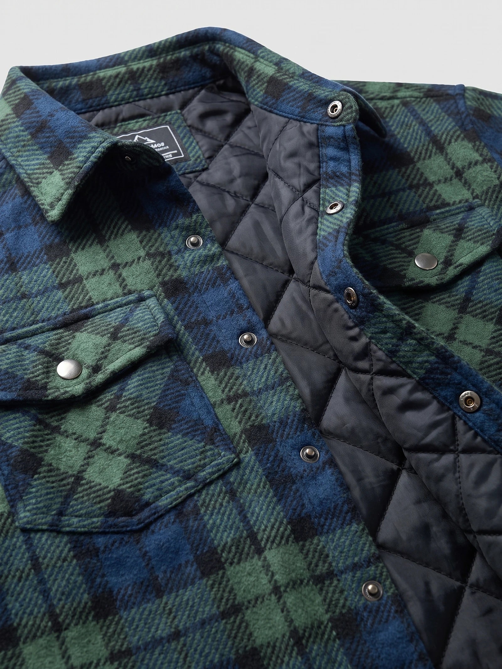 Close-up of the Green plaid Flannel Jacket showing the pointed collar, snap-button placket, chest pocket, and quilted lining.