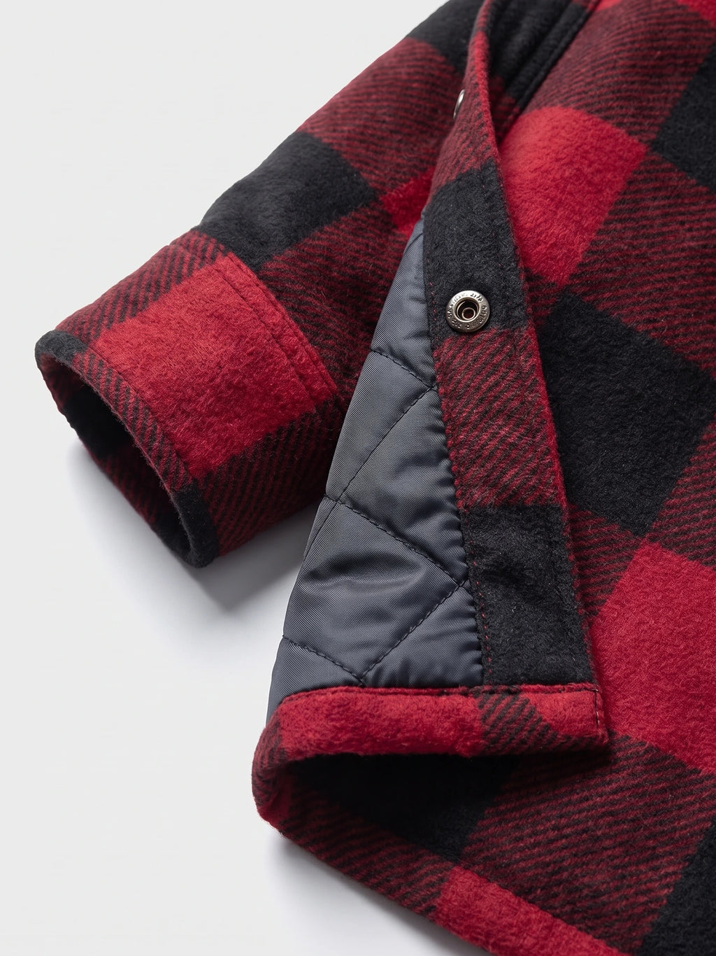 Close-up of the Red men’s Flannel Jacket showing the plaid sleeve, snap button, and quilted lining.