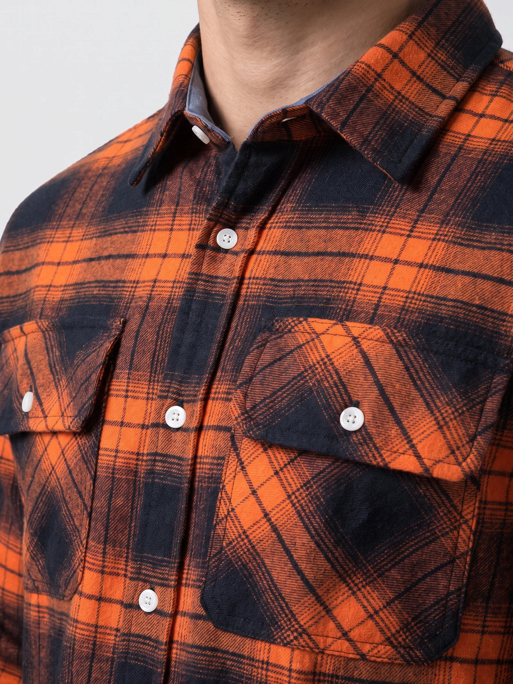 Close-up of an Orange plaid flannel shirt jacket with a button-down collar, front placket, and flap chest pockets.