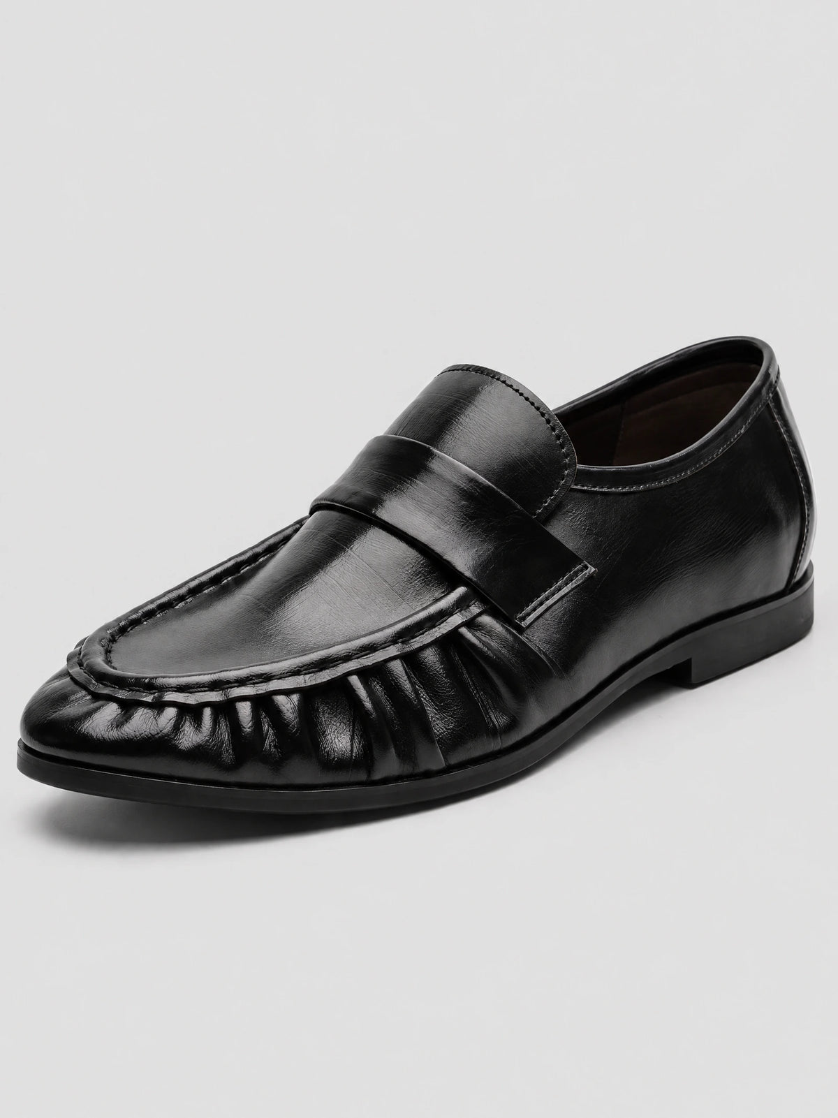 Three-quarter view of a Black leather ruched loafer with a wide vamp strap, moc-toe stitching, and low sole.