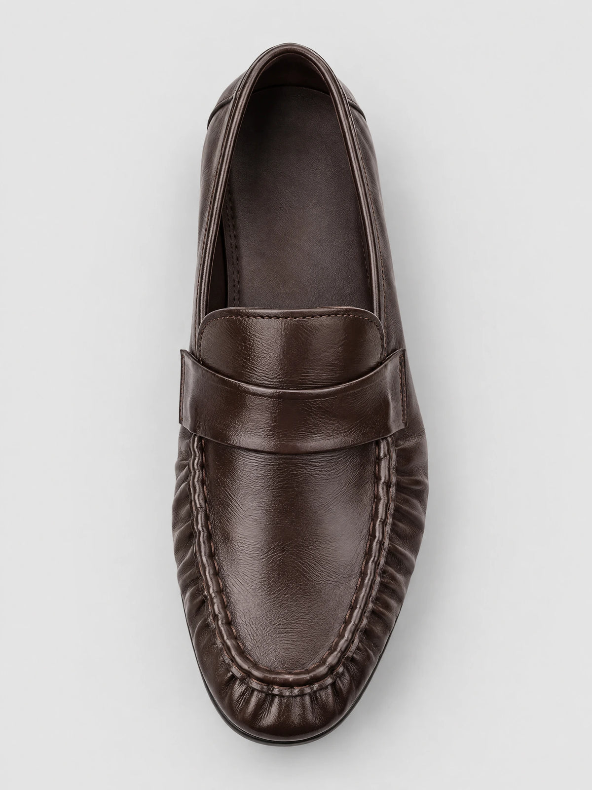 Top-down close-up of a Brown ruched leather loafer with a stitched moc toe and saddle strap.