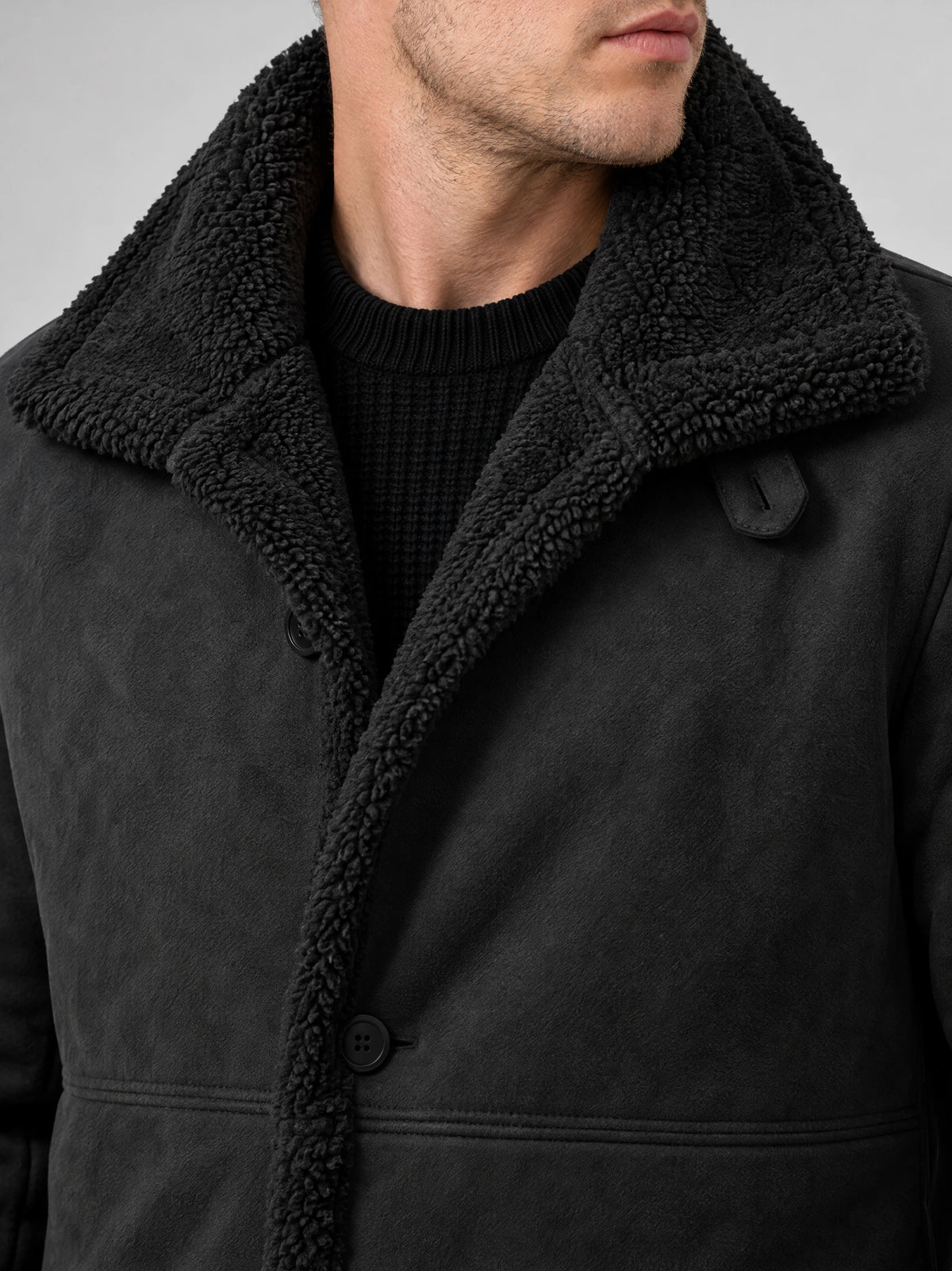 Close-up of a Black Sherpa-lined jacket showing the textured collar, button front, and adjustable throat tab.