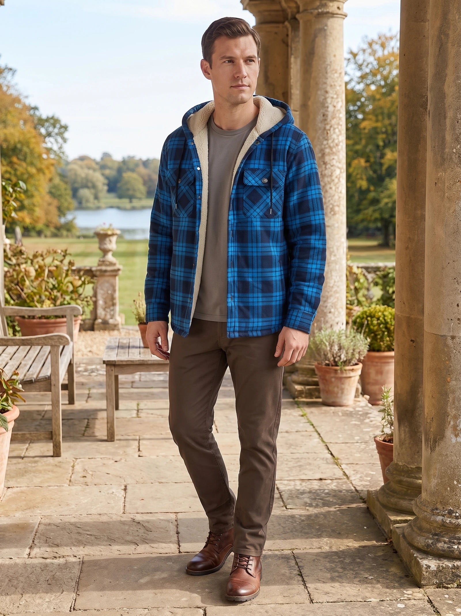 Model wearing a Blue Sherpa Lined Jacket with a hood and plaid pattern on a stone terrace beside a garden.
