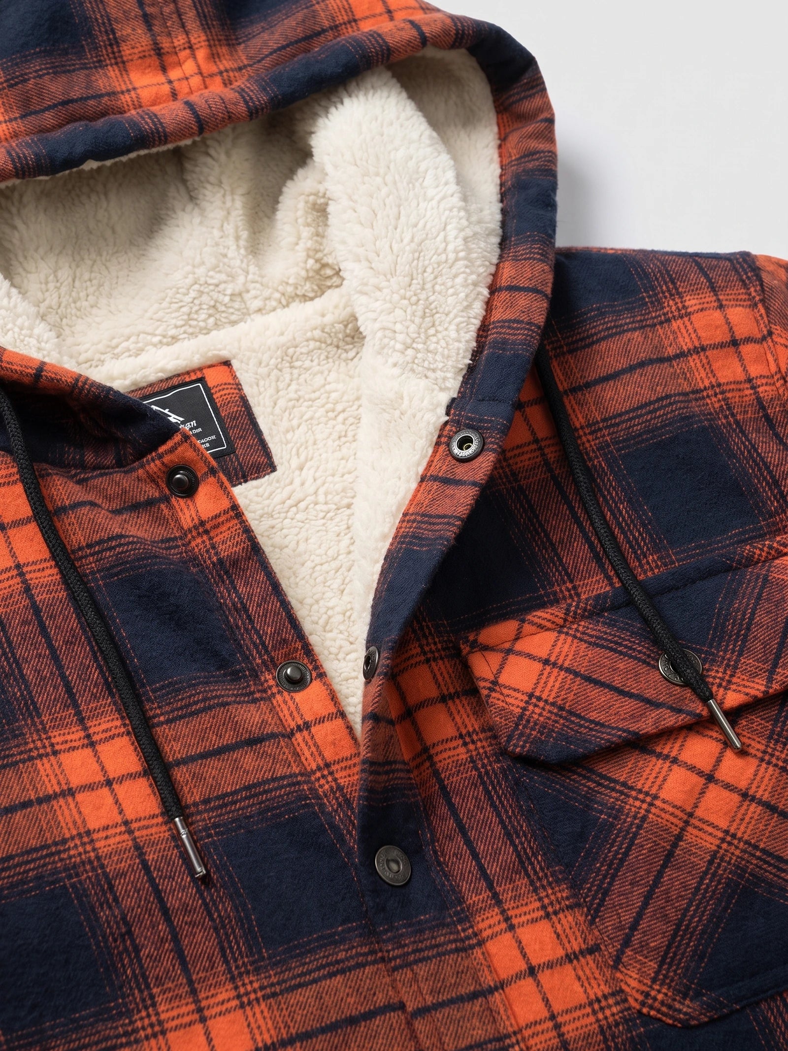 Close-up of the Orange Sherpa Lined Jacket showing the hood’s soft sherpa interior, snap-button placket, drawstrings, and plaid fabric.