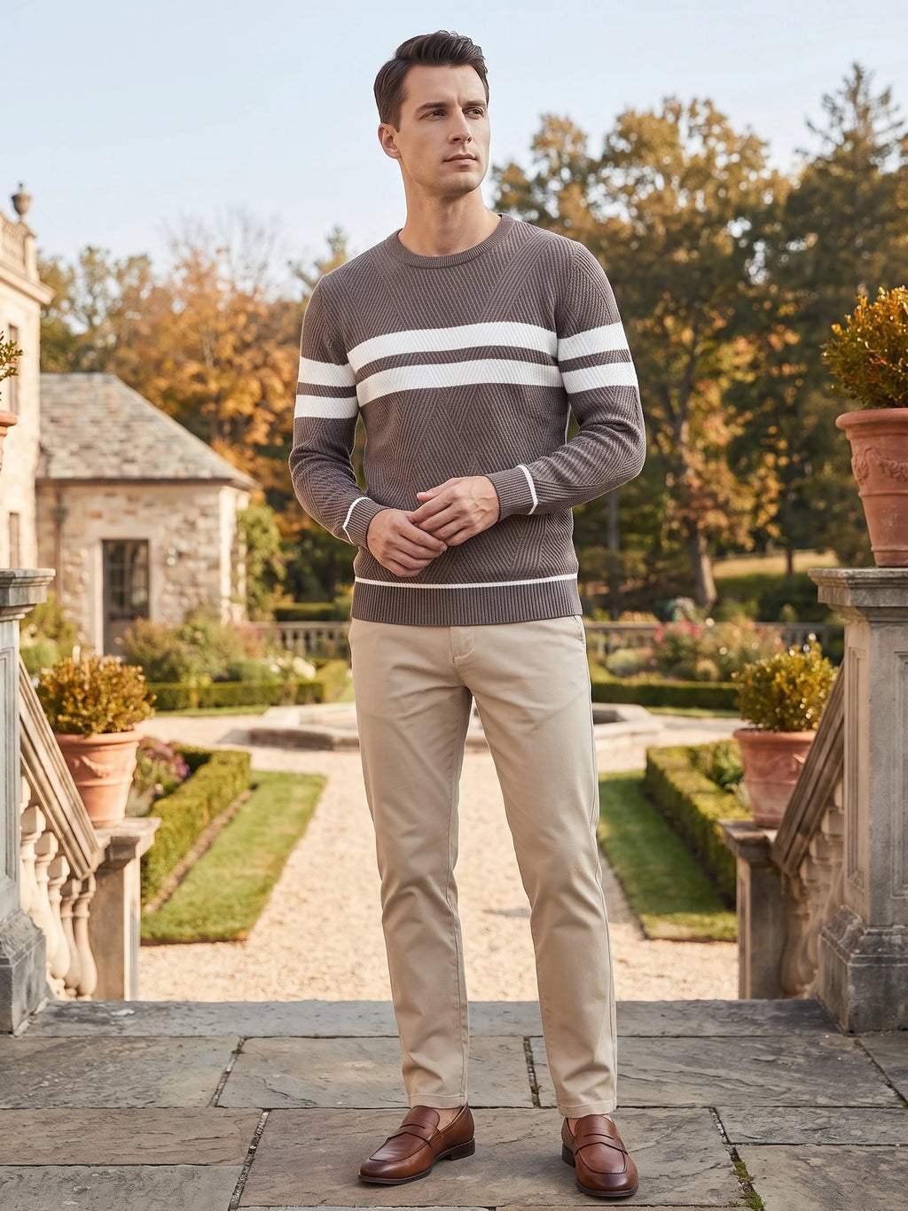 Model wearing a Brown slim crew-neck sweater with contrasting striped panels while standing on a garden terrace.