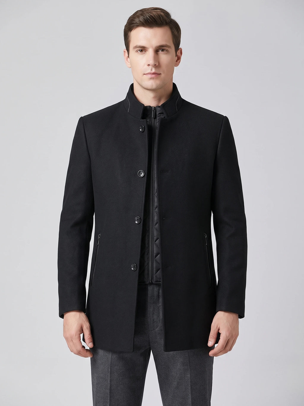 Front studio view of a model wearing a Black wool overcoat with a stand collar, button closure, zippered pockets, and quilted inner layer.