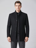 Front studio view of a model wearing a Black wool overcoat with a stand collar, button closure, zippered pockets, and quilted inner layer.