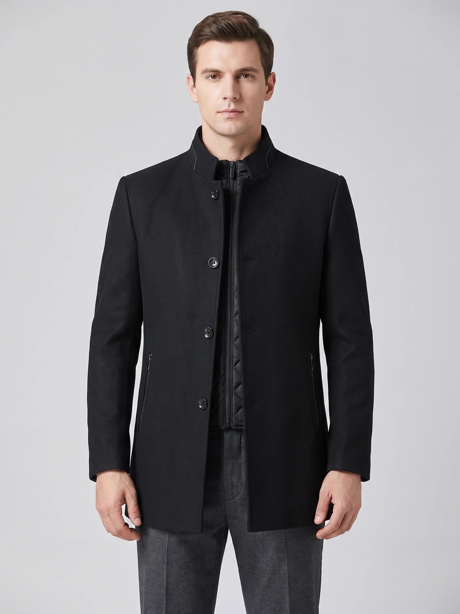 Front studio view of a model wearing a Black wool overcoat with a stand collar, button closure, zippered pockets, and quilted inner layer.