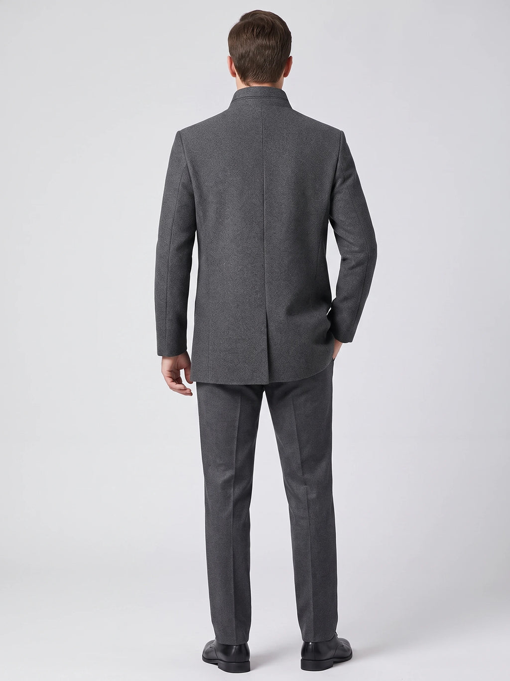 Rear studio view of a model wearing a Gray wool overcoat with a stand collar and center back seam.
