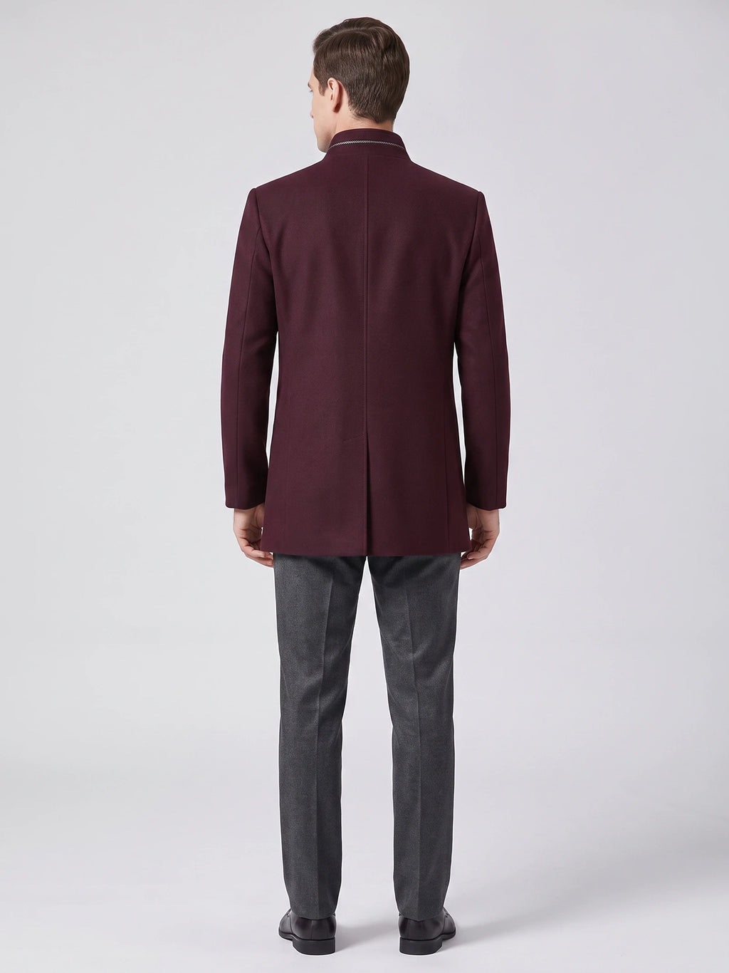Rear studio view of a model wearing a Wine wool overcoat with a stand collar and center back vent.