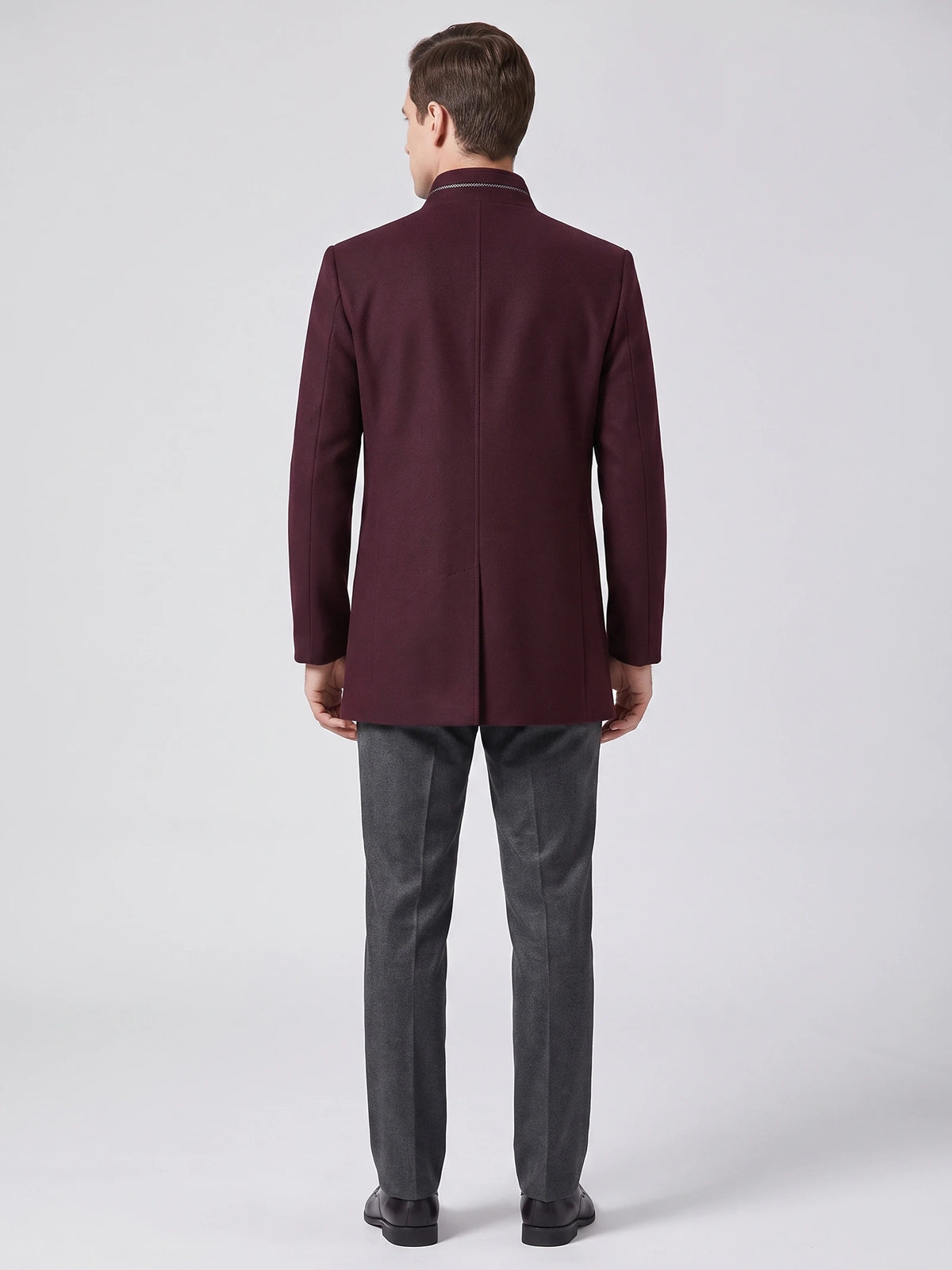 Rear studio view of a model wearing a Wine wool overcoat with a stand collar and center back vent.