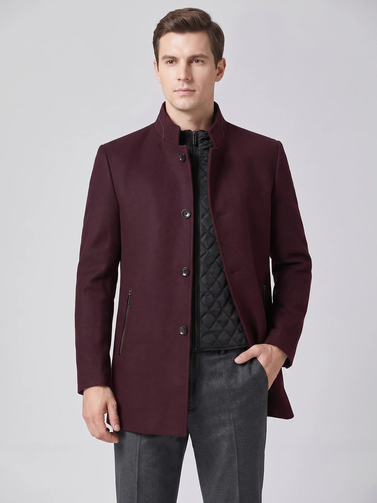 Front studio view of a model wearing a Wine wool overcoat with a stand collar, button front, zip pockets, and quilted inner layer.