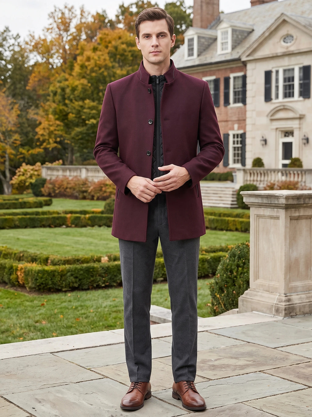 Man wearing a Wine wool overcoat with a stand collar while standing outside a large home.