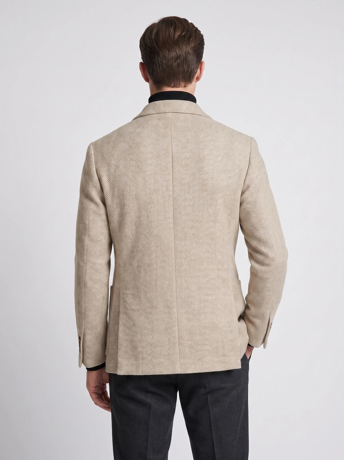 Rear view of a model wearing a Beige wool Men Suit Coat with a herringbone pattern and center back seam.