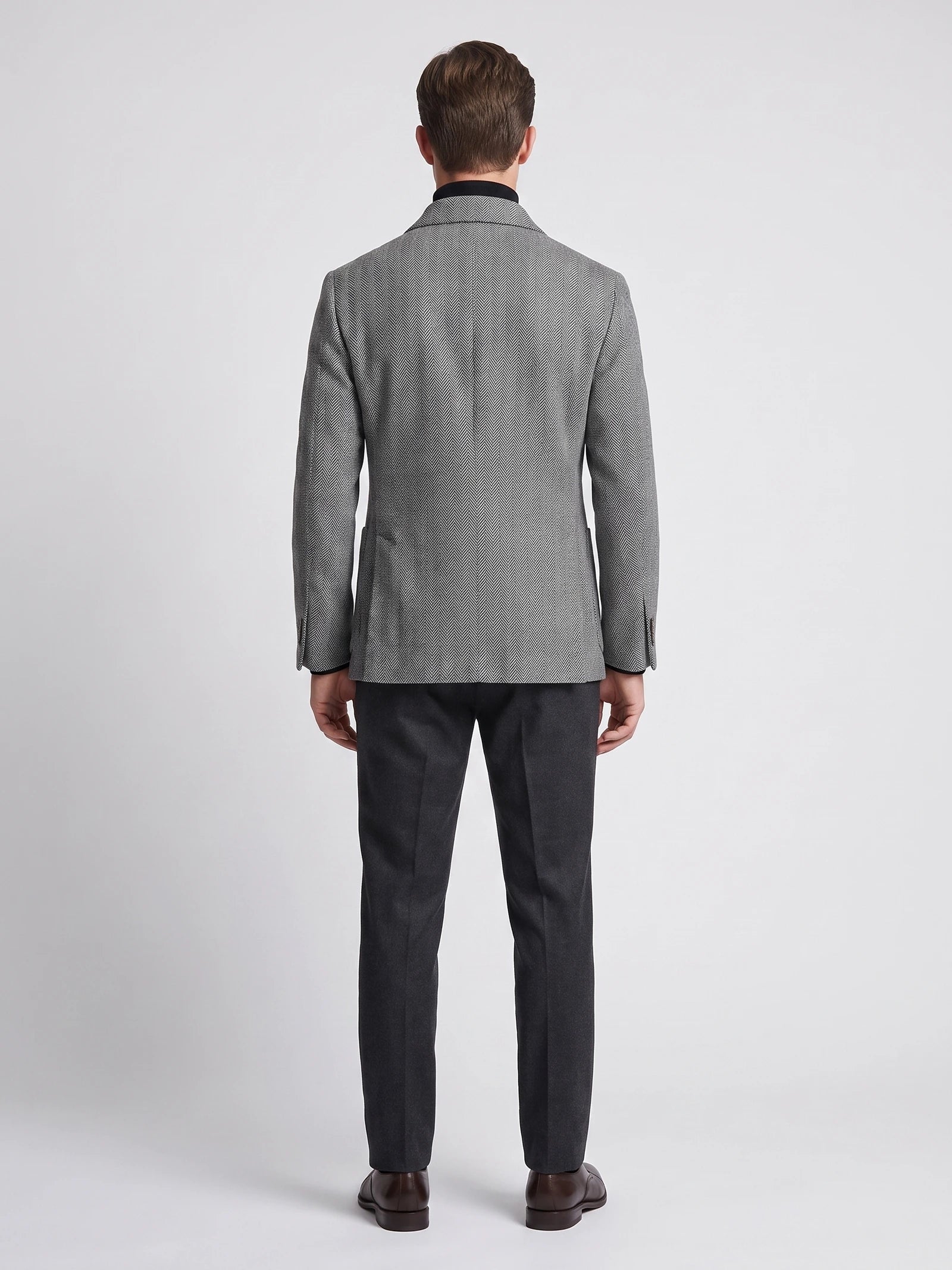 Rear studio view of a model wearing a Gray wool Men Suit Coat with a herringbone pattern.