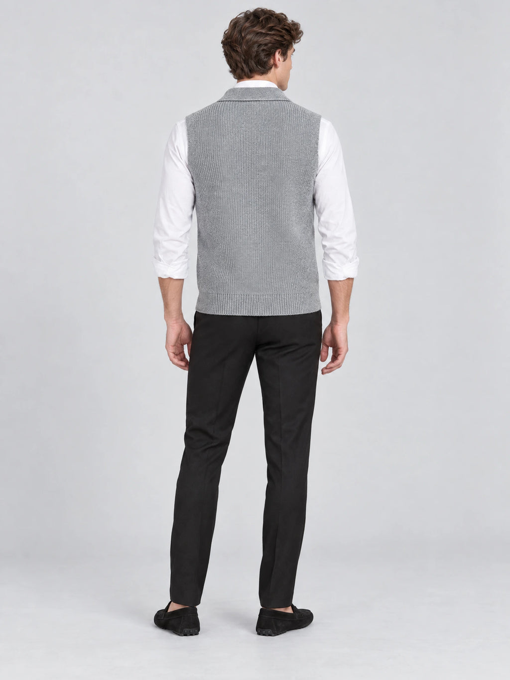 Rear studio view of a model wearing a Gray cotton knit Sweater Vest with a ribbed hem over a long-sleeve shirt.
