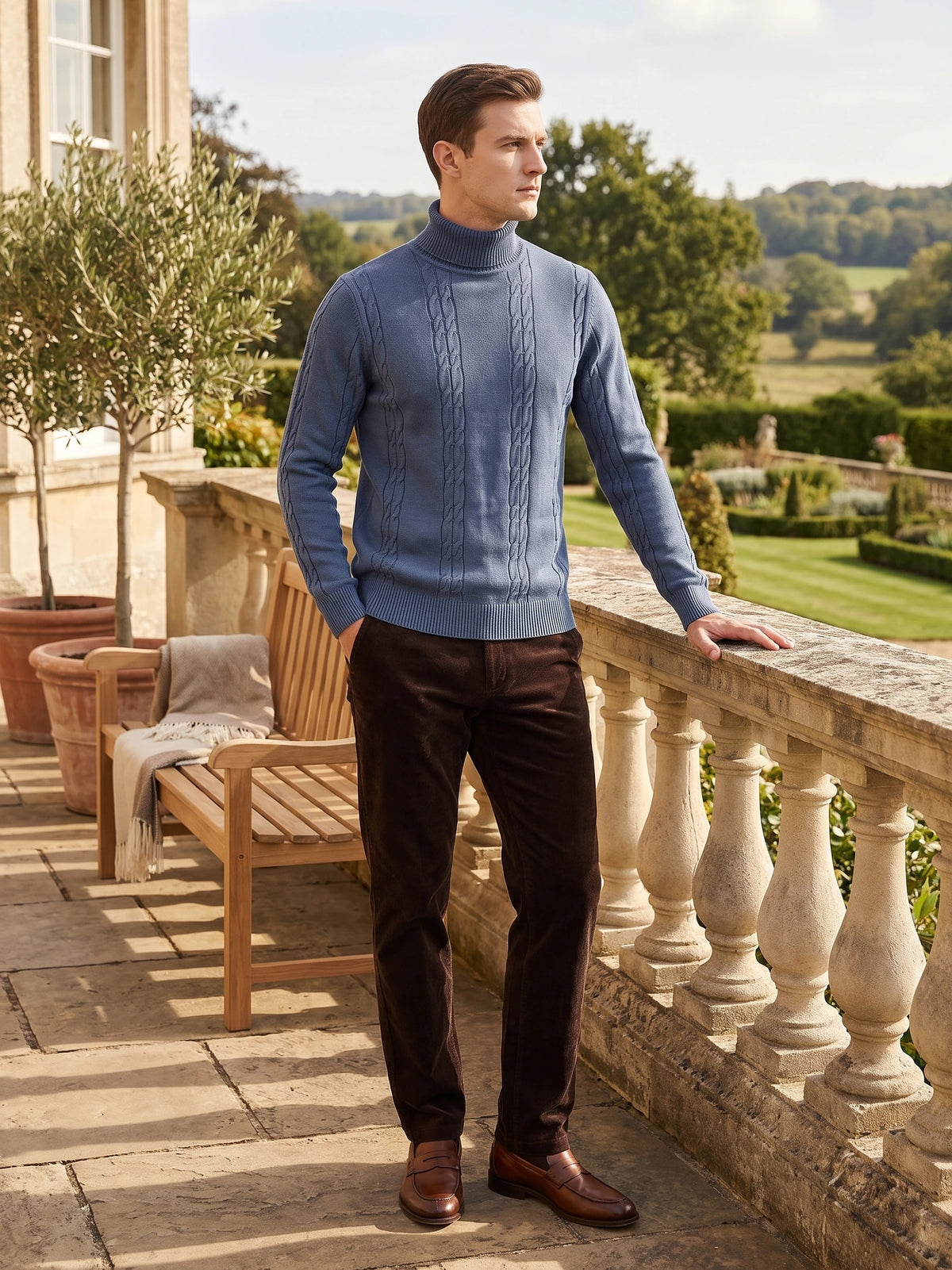Man wearing a Blue cable-knit cotton Turtleneck Sweater on a terrace overlooking a landscaped garden.