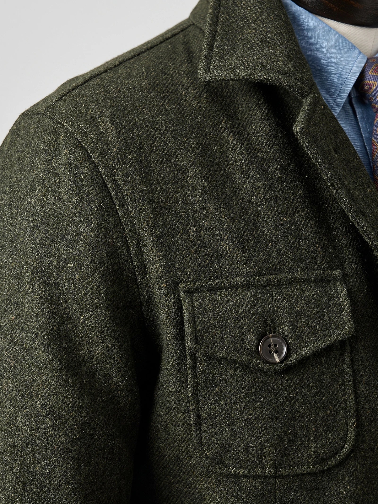 Close-up of the Green Tweed Jacket showing the notched lapel, textured fabric, flap pocket, and button closure.