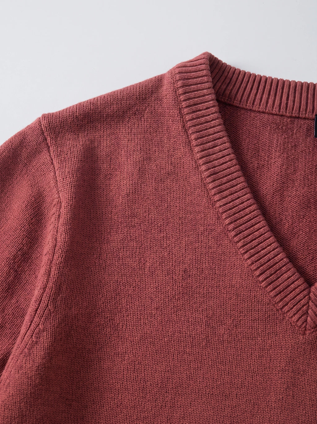 Close-up of the ribbed V-neck and fine cotton knit texture on a Red men's sweater.