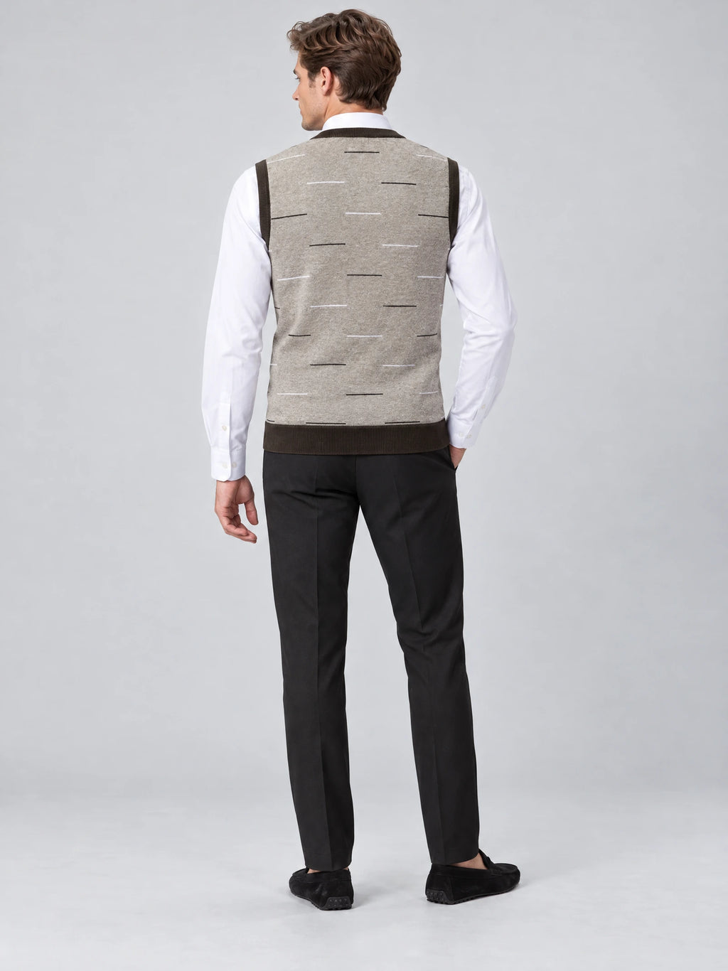 Rear studio view of a model wearing a Beige v neck sweater vest with a scattered dash pattern over a dress shirt.