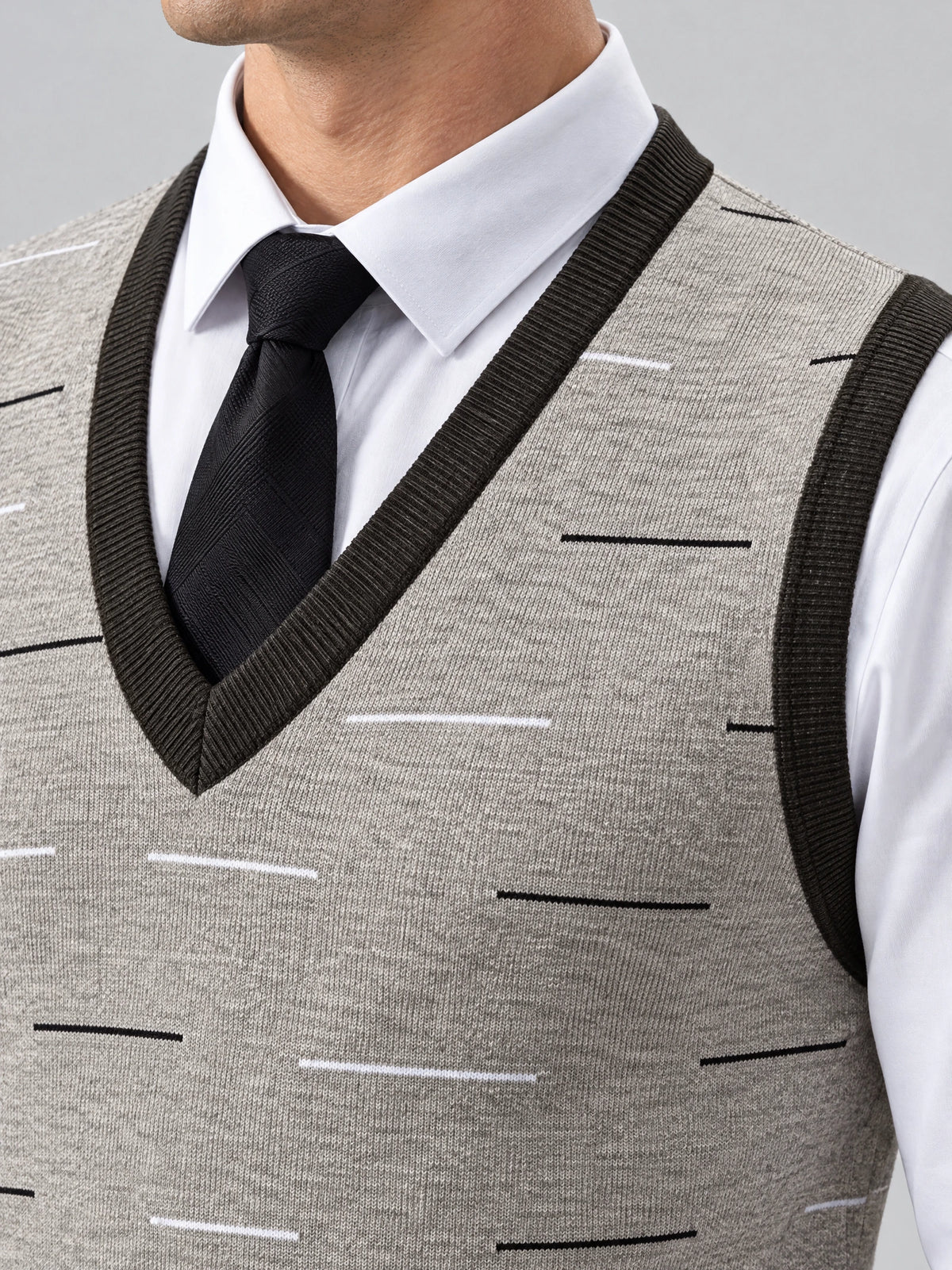 Close-up of a Beige v neck sweater vest with ribbed trim and a geometric knit pattern, layered over a dress shirt and tie.
