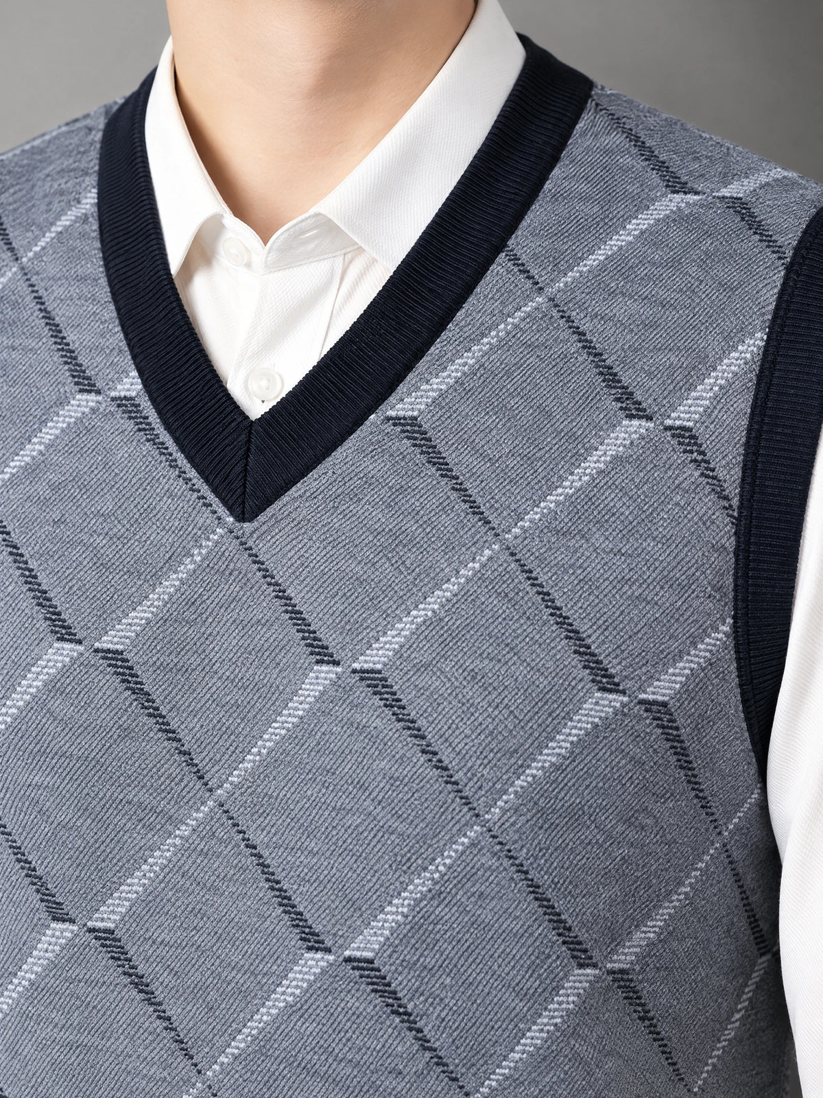 Close-up of a Gray v neck sweater vest with ribbed trim and an argyle knit pattern layered over a collared shirt.
