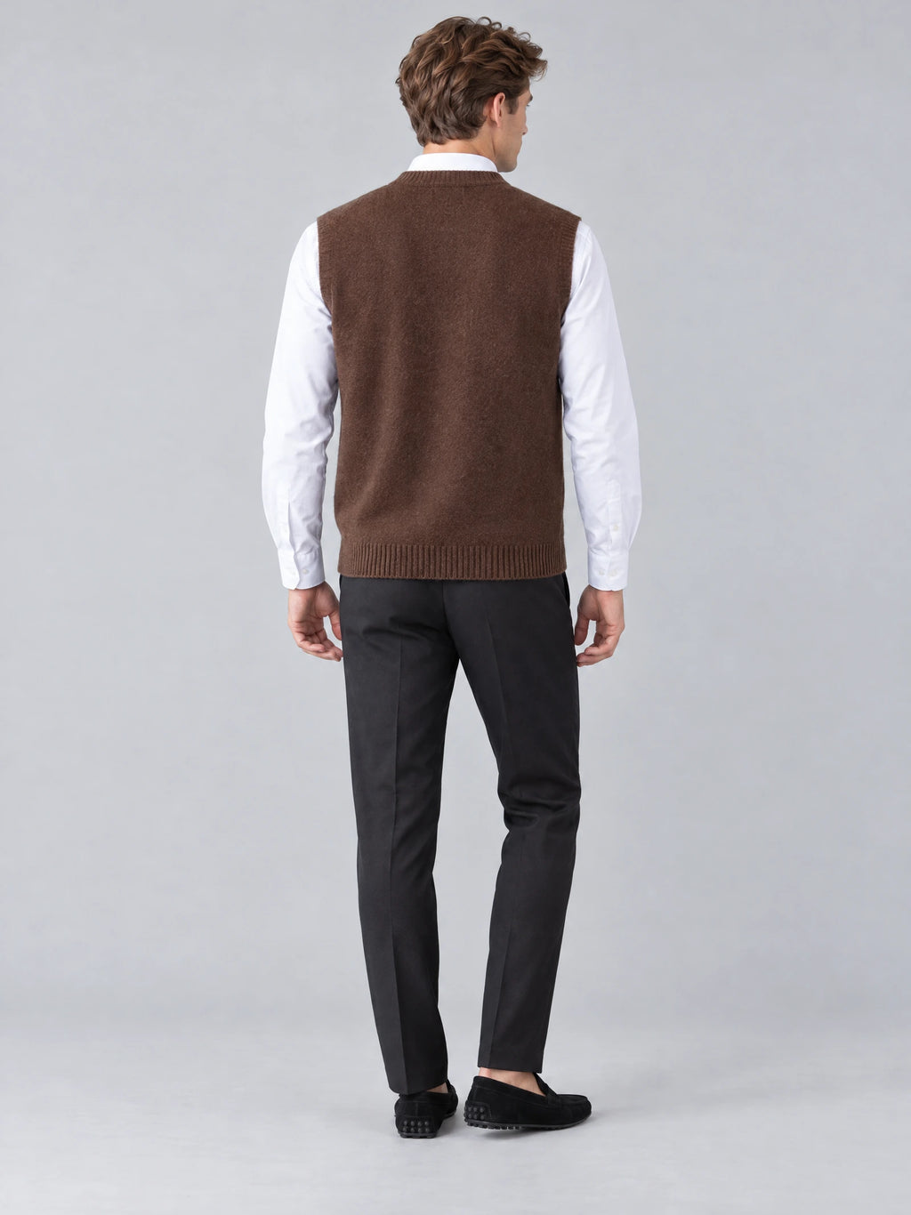 Rear studio view of a model wearing a Brown wool v neck sweater vest with ribbed hem.