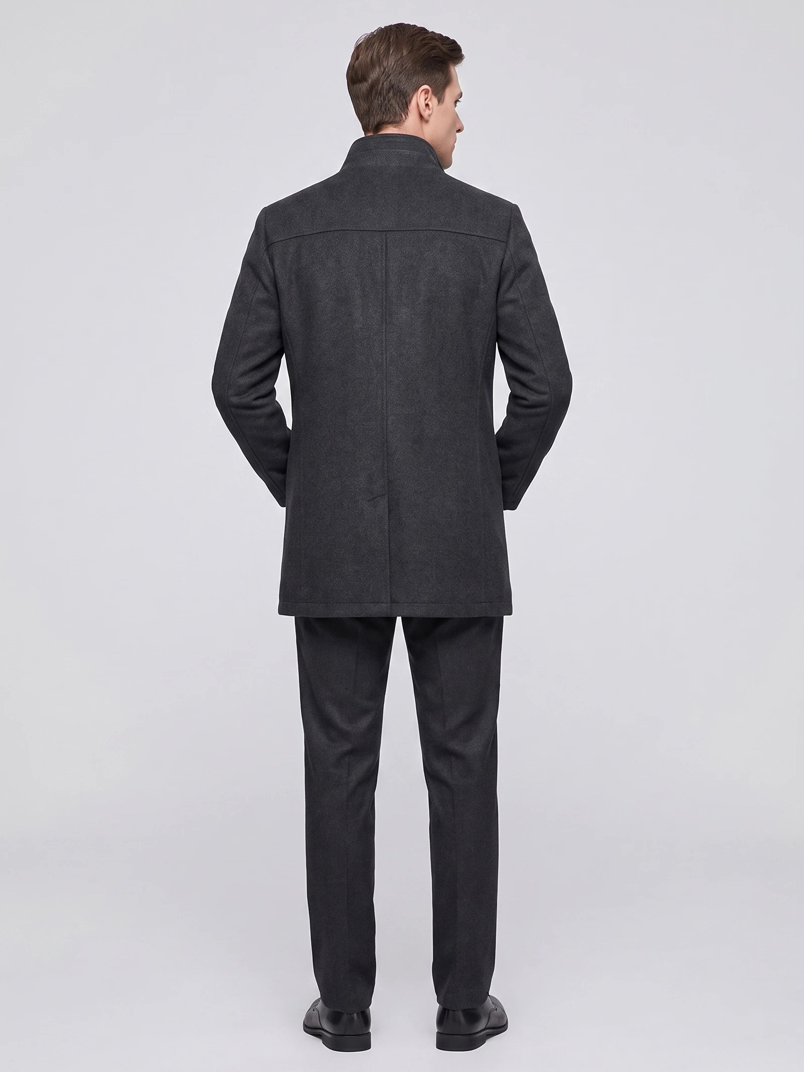 Rear studio view of a model wearing a Gray wool overcoat with a stand collar, back yoke, and center back seam.