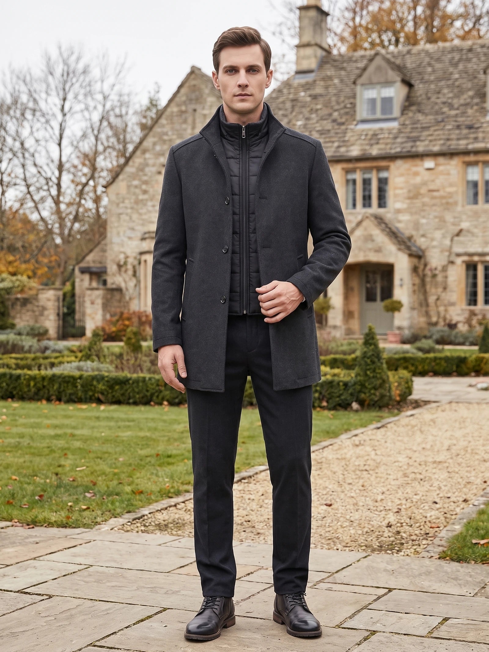 Man wearing a Gray wool overcoat over a zip-front layer while standing on a garden path outside a stone house.