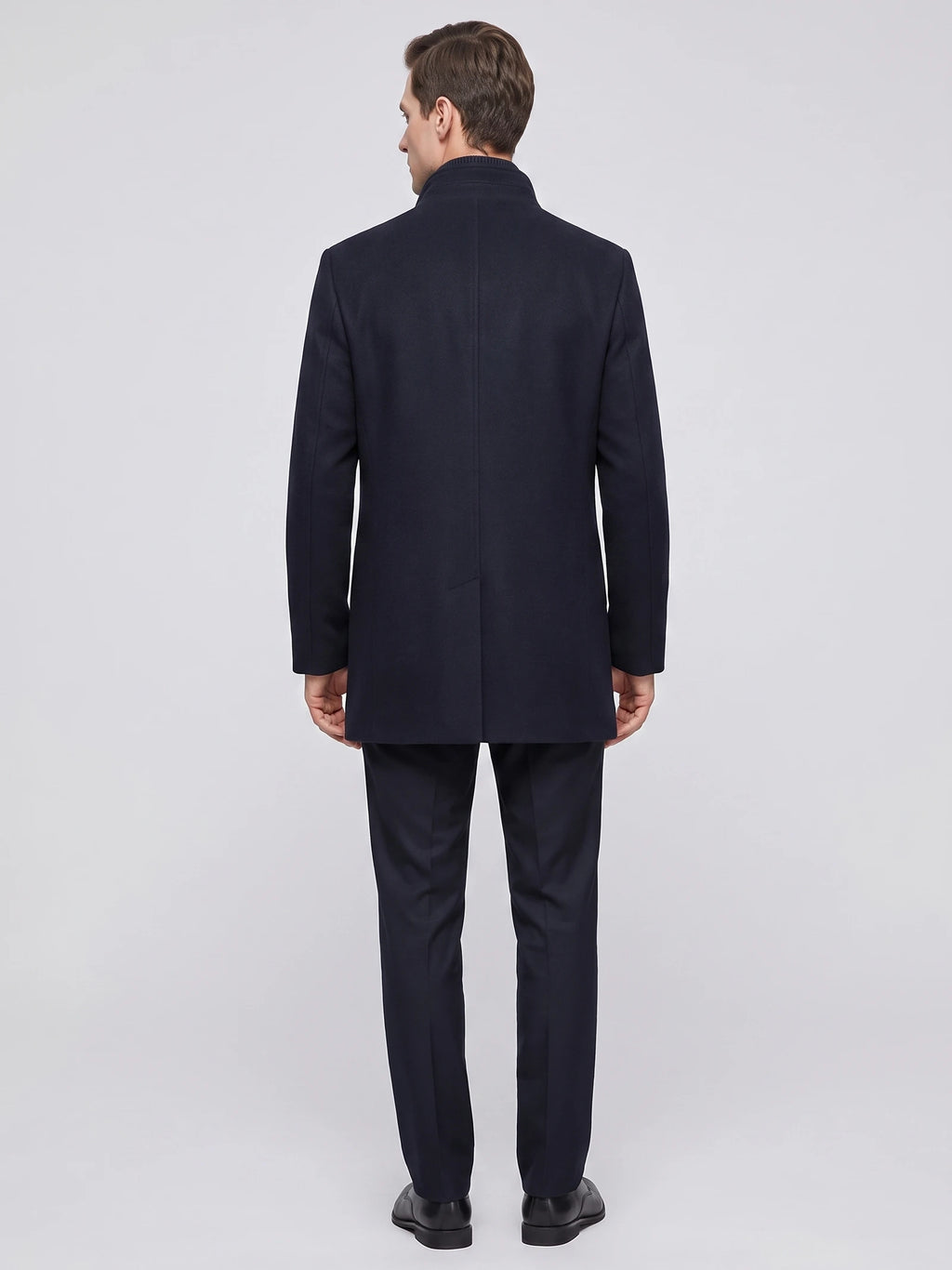 Rear studio view of a model wearing a Navy wool overcoat with a stand collar and center back vent.
