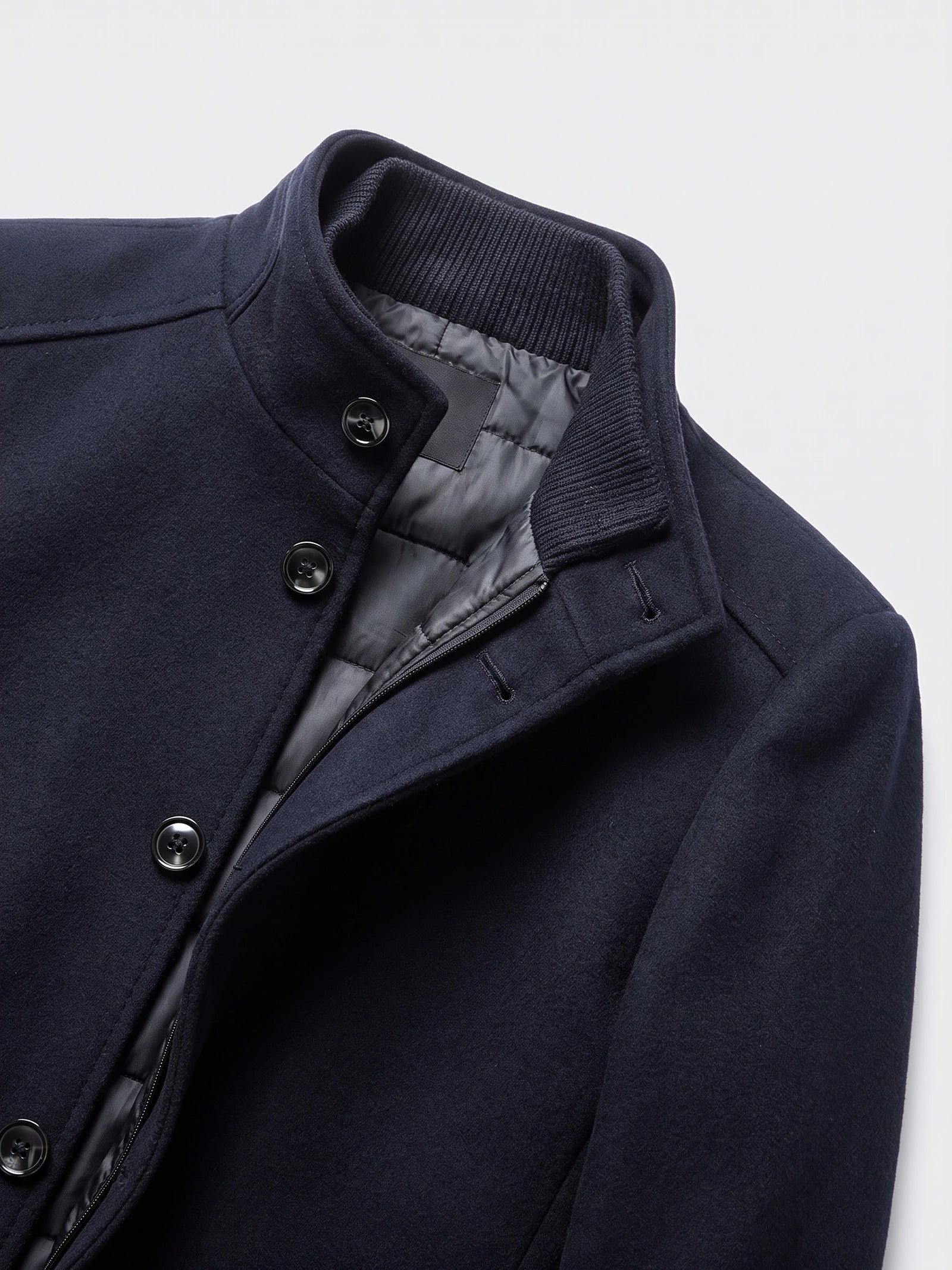 Close-up of a Navy wool overcoat with a ribbed stand collar, buttoned front, and quilted inner lining.