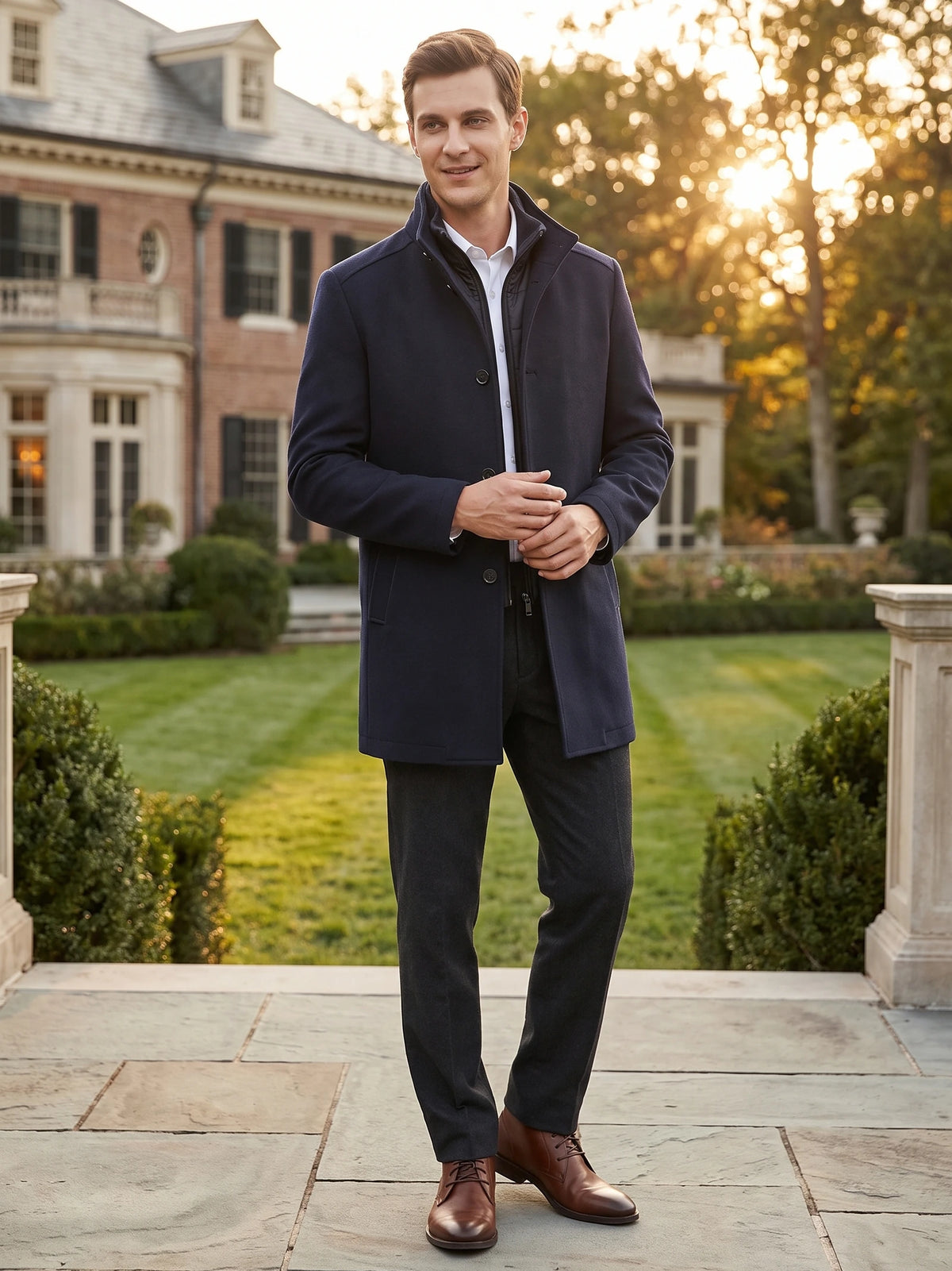 Man wearing a Navy wool overcoat with a stand collar on a sunlit estate walkway.