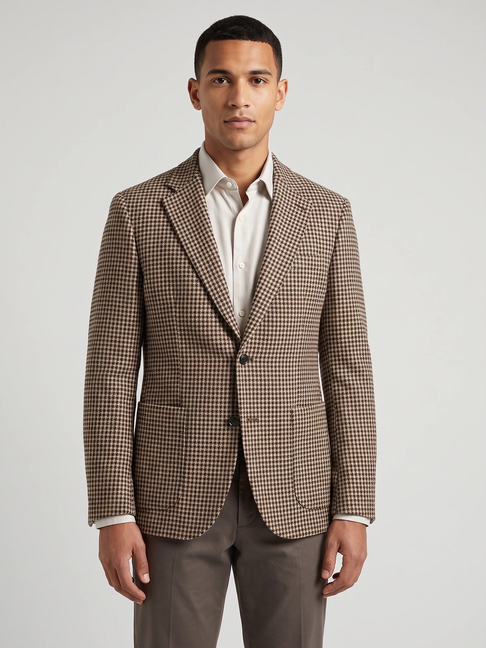 Front studio view of a model wearing a Brown wool tweed blazer with a houndstooth pattern, notch lapels, and flap pockets.