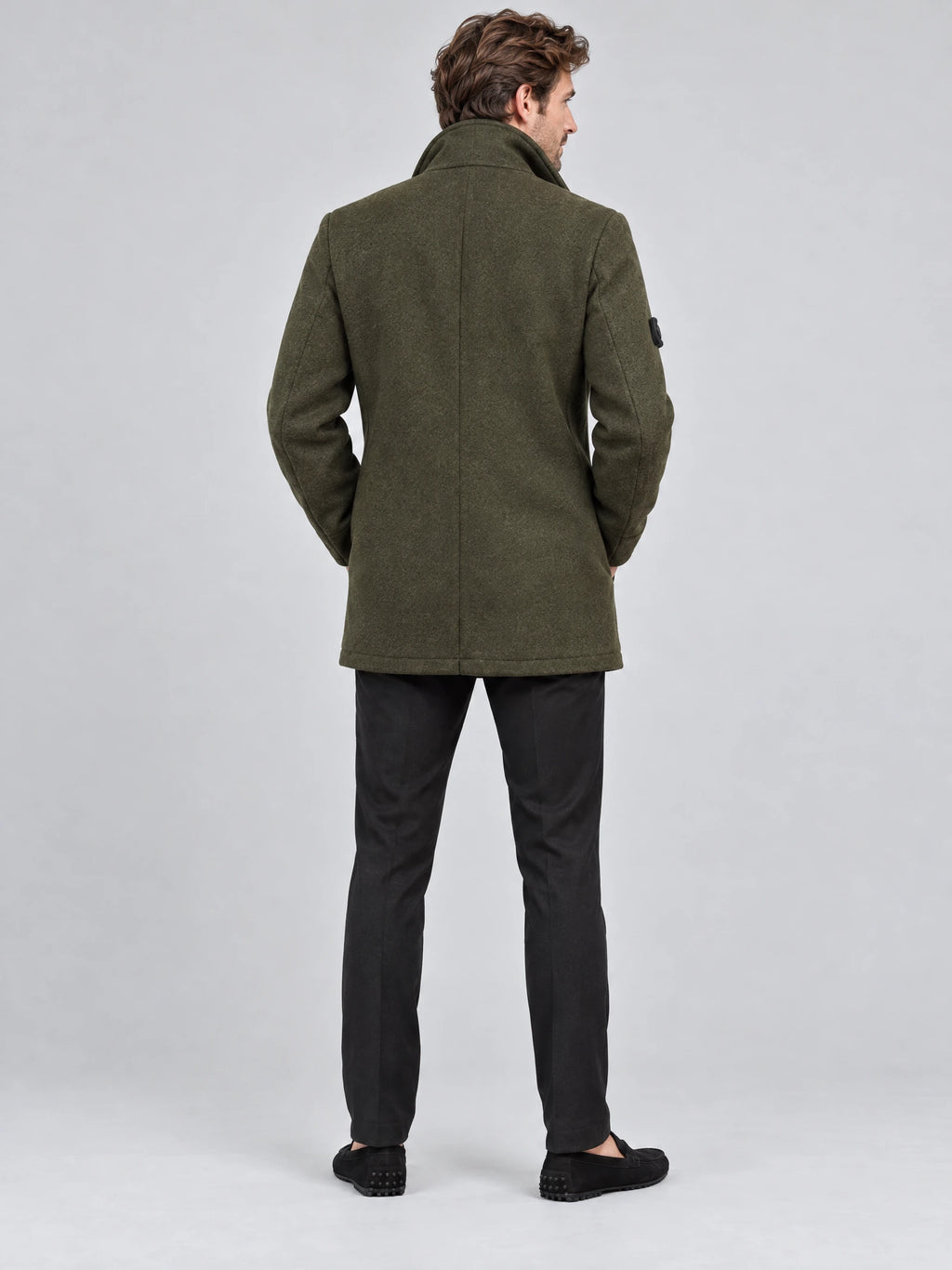 Rear studio view of a model wearing a Green wool winter coat with a raised collar and center back seam.