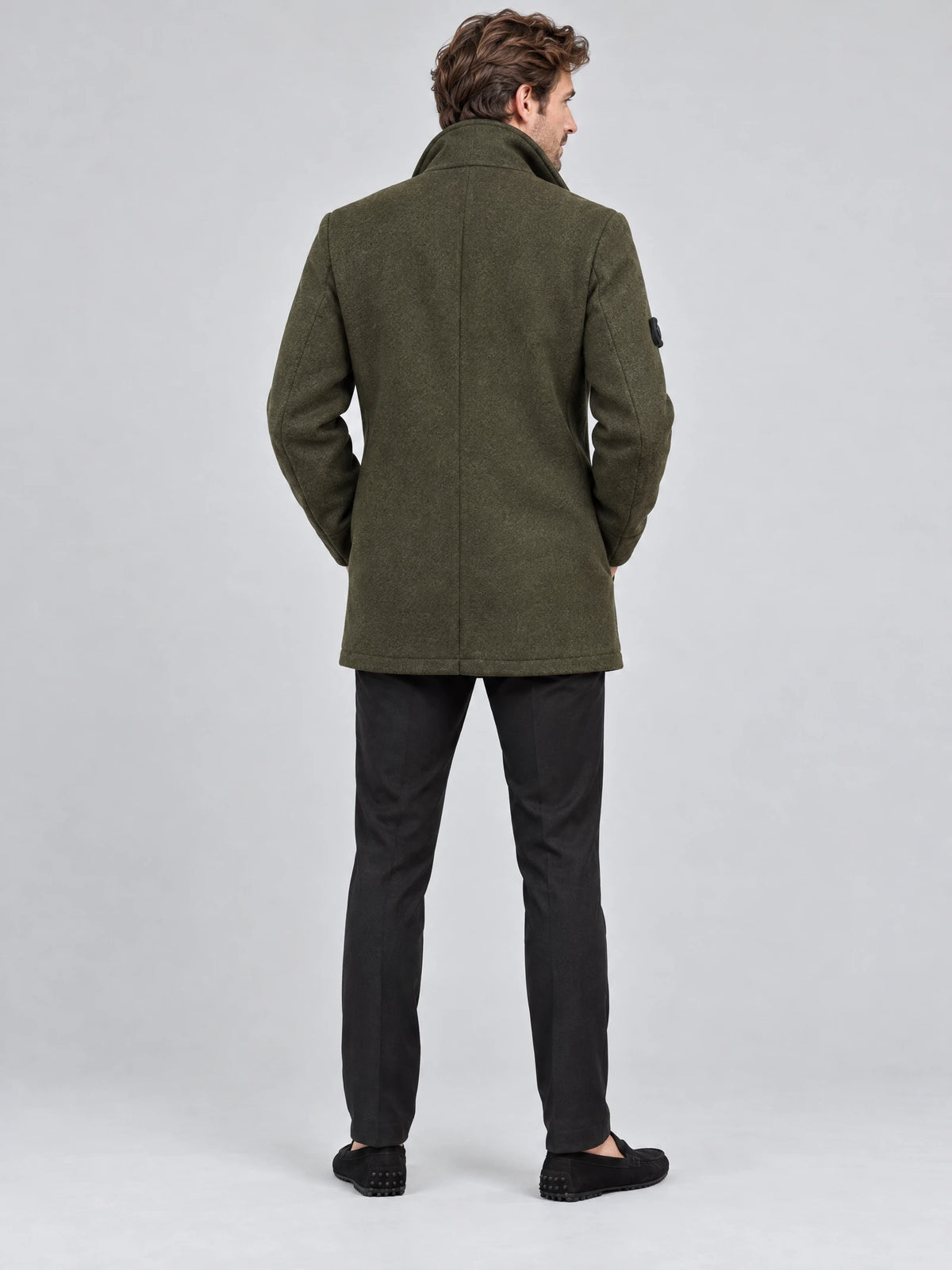 Rear studio view of a model wearing a Green wool winter coat with a raised collar and center back seam.