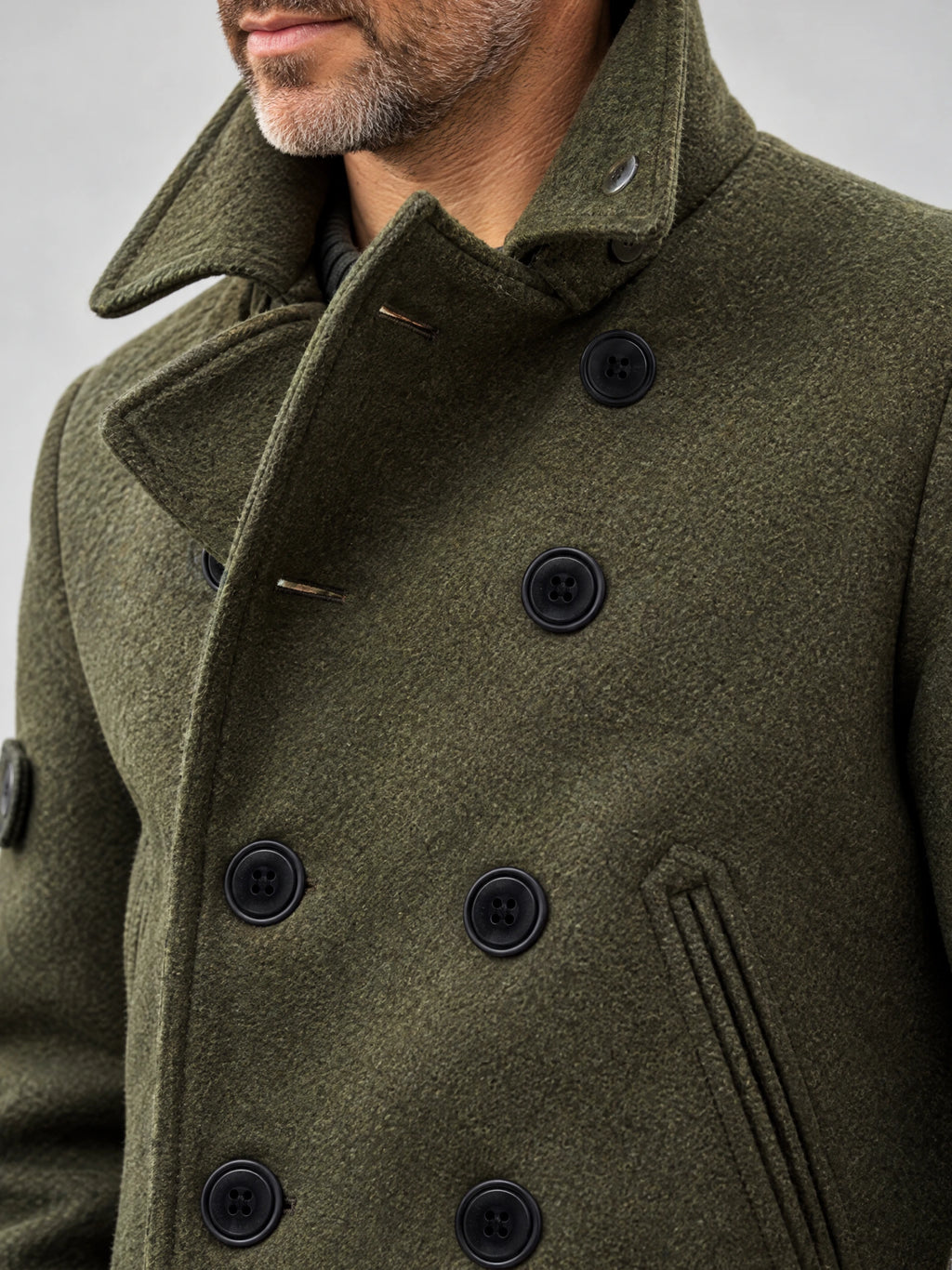 Close-up of a Green men's Wool Winter Coat showing its textured fabric, wide collar, double-breasted buttons, and welt pocket.