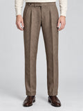 Front studio view of a model wearing Brown woolen herringbone pattern formal pants with a buttoned waist, pleats, and cuffed hems.