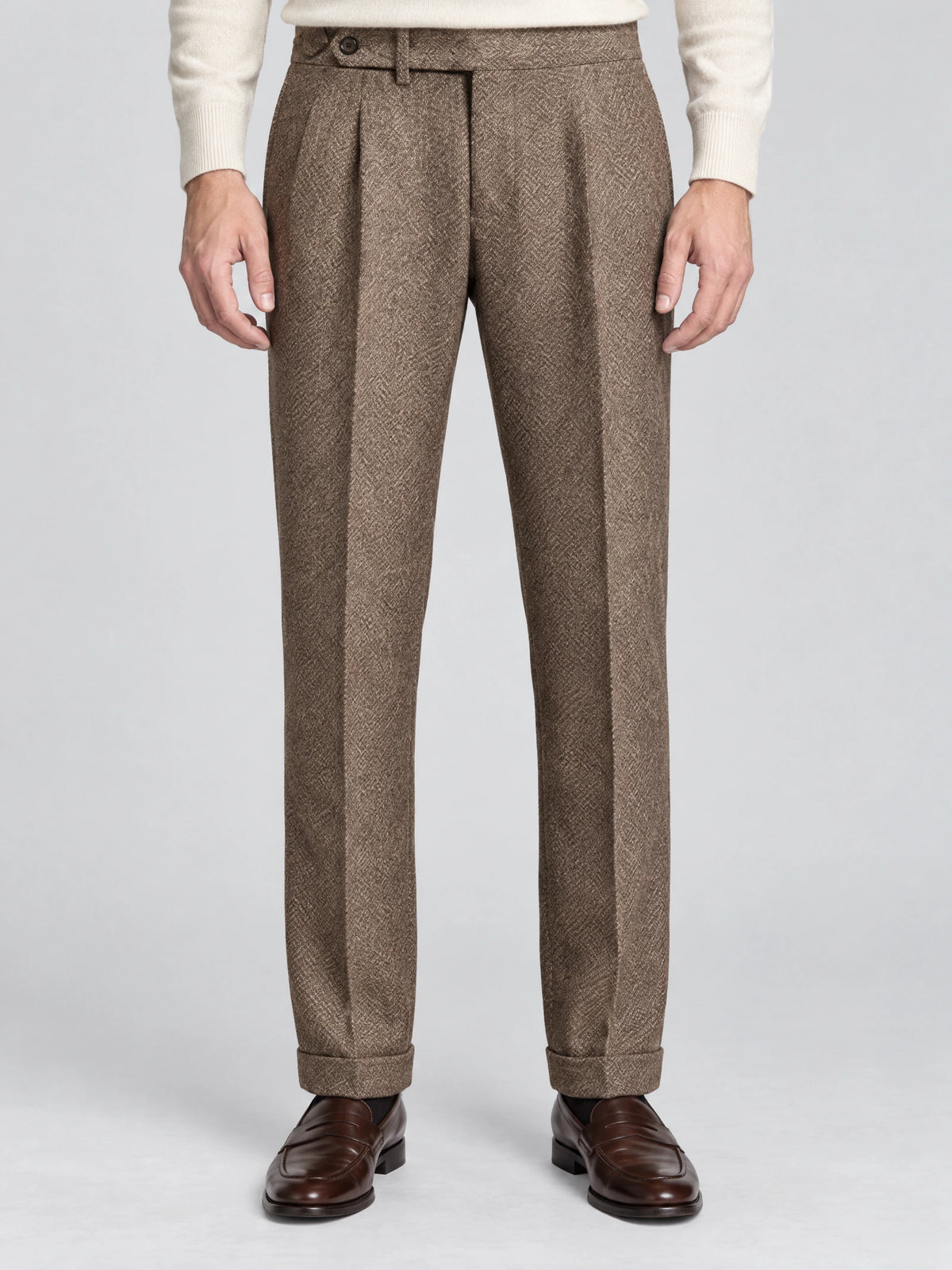 Front studio view of a model wearing Brown woolen herringbone pattern formal pants with a buttoned waist, pleats, and cuffed hems.