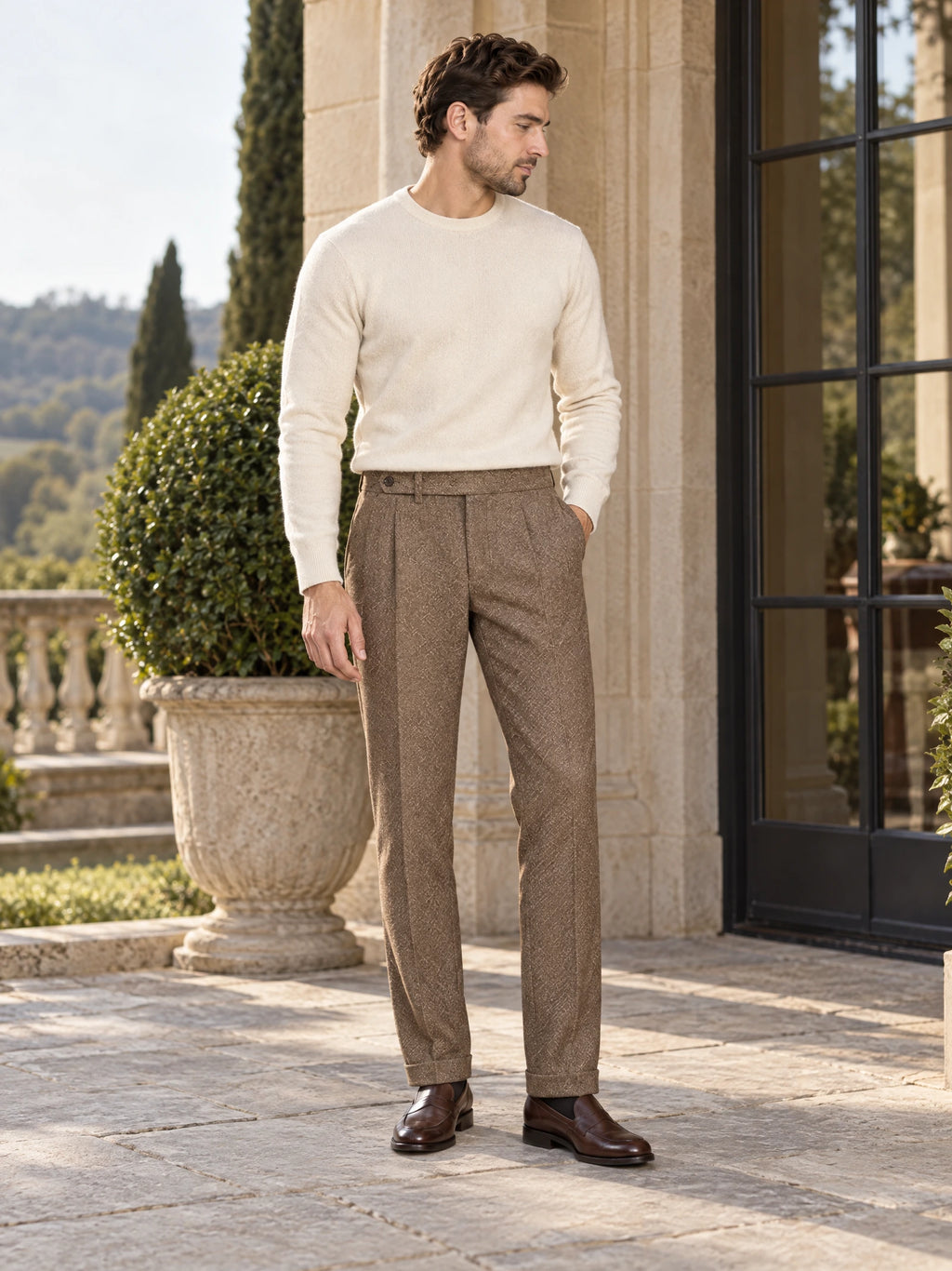 Model wearing Brown woolen herringbone pattern formal pants with a cuffed hem on a sunlit stone terrace.