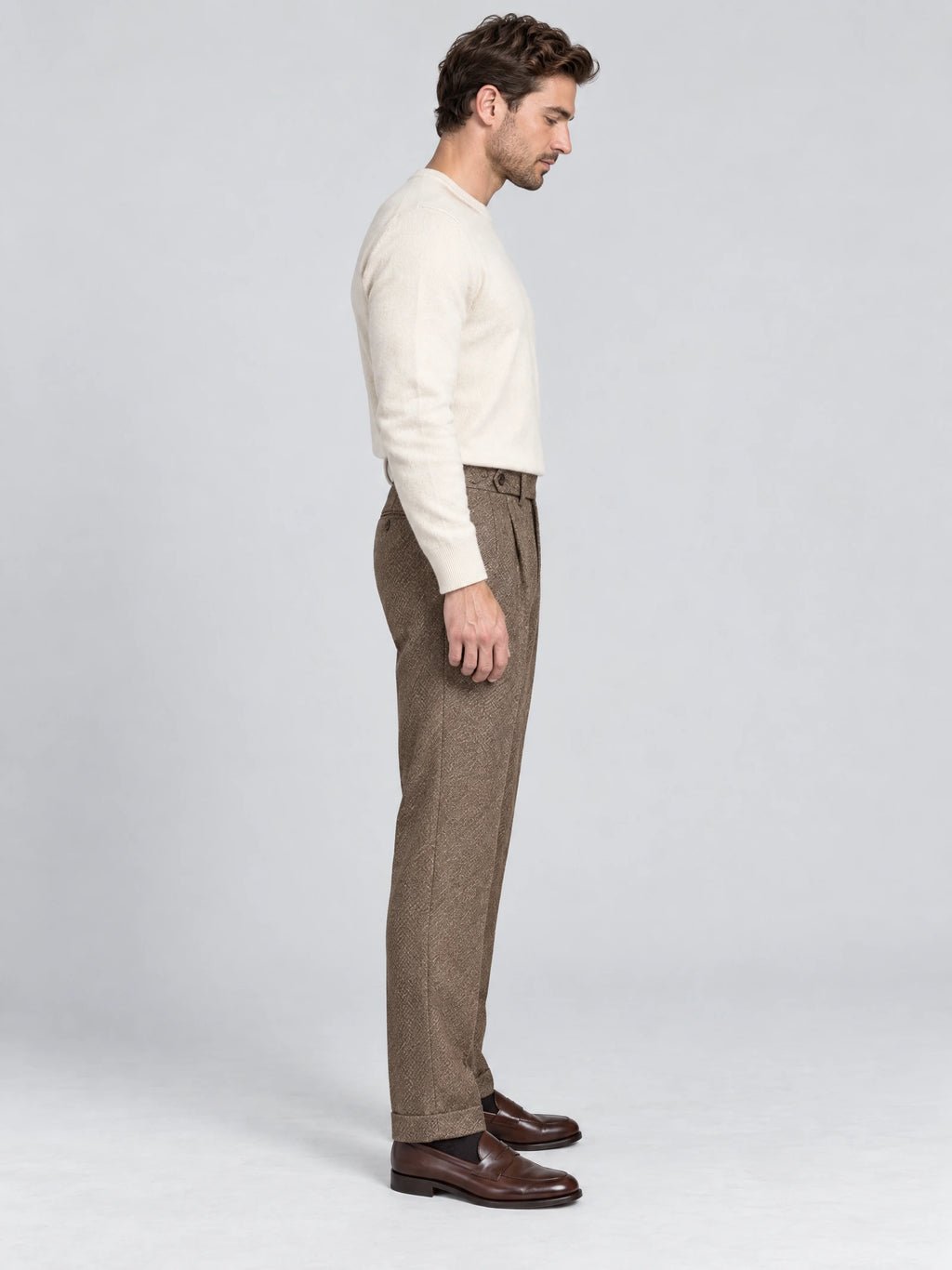 Side studio view of a model wearing Brown woolen herringbone pattern formal pants with a high waist and cuffed hems.