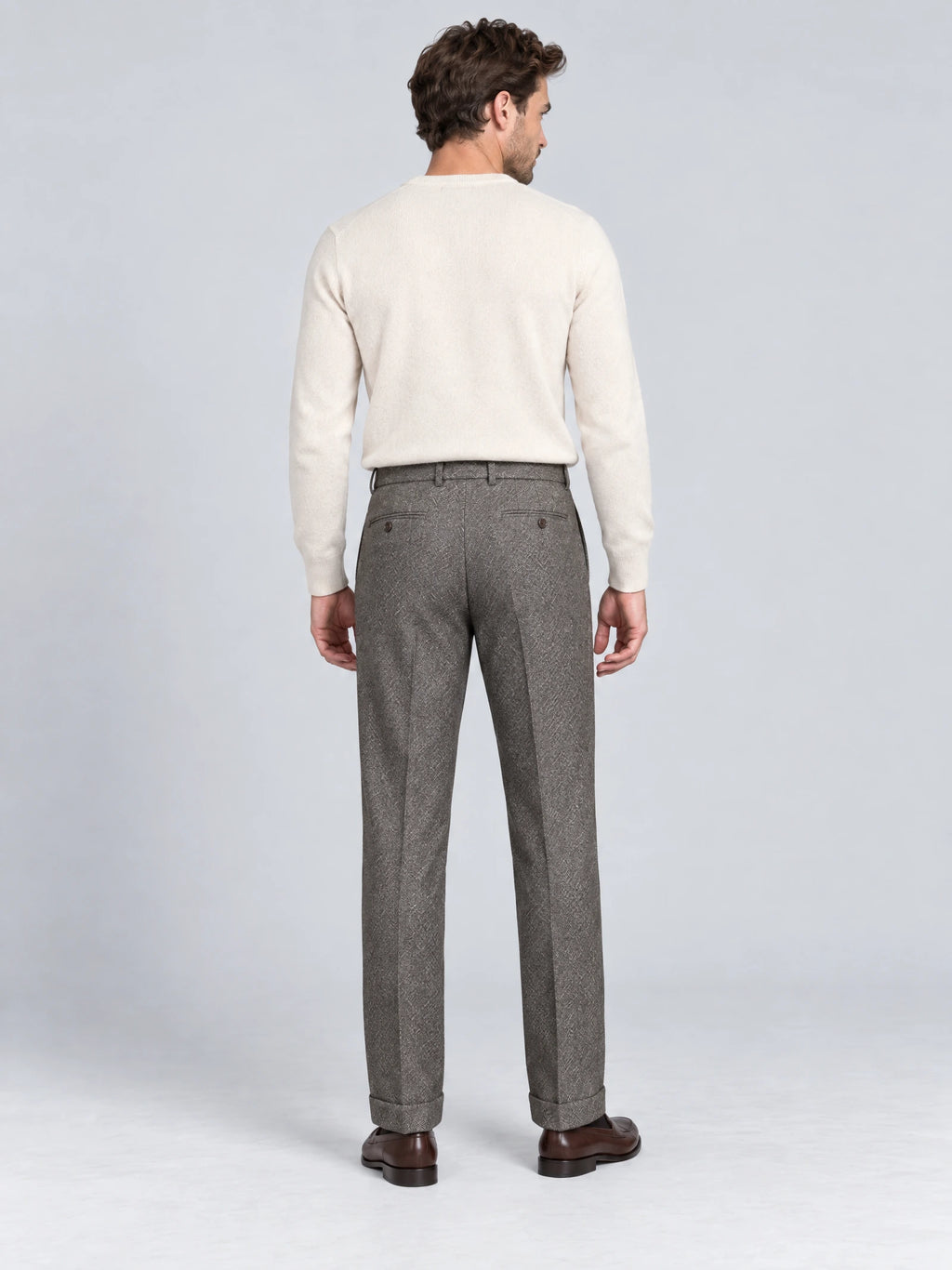 Rear studio view of a model wearing Gray woolen herringbone formal pants with buttoned back pockets and cuffed hems.