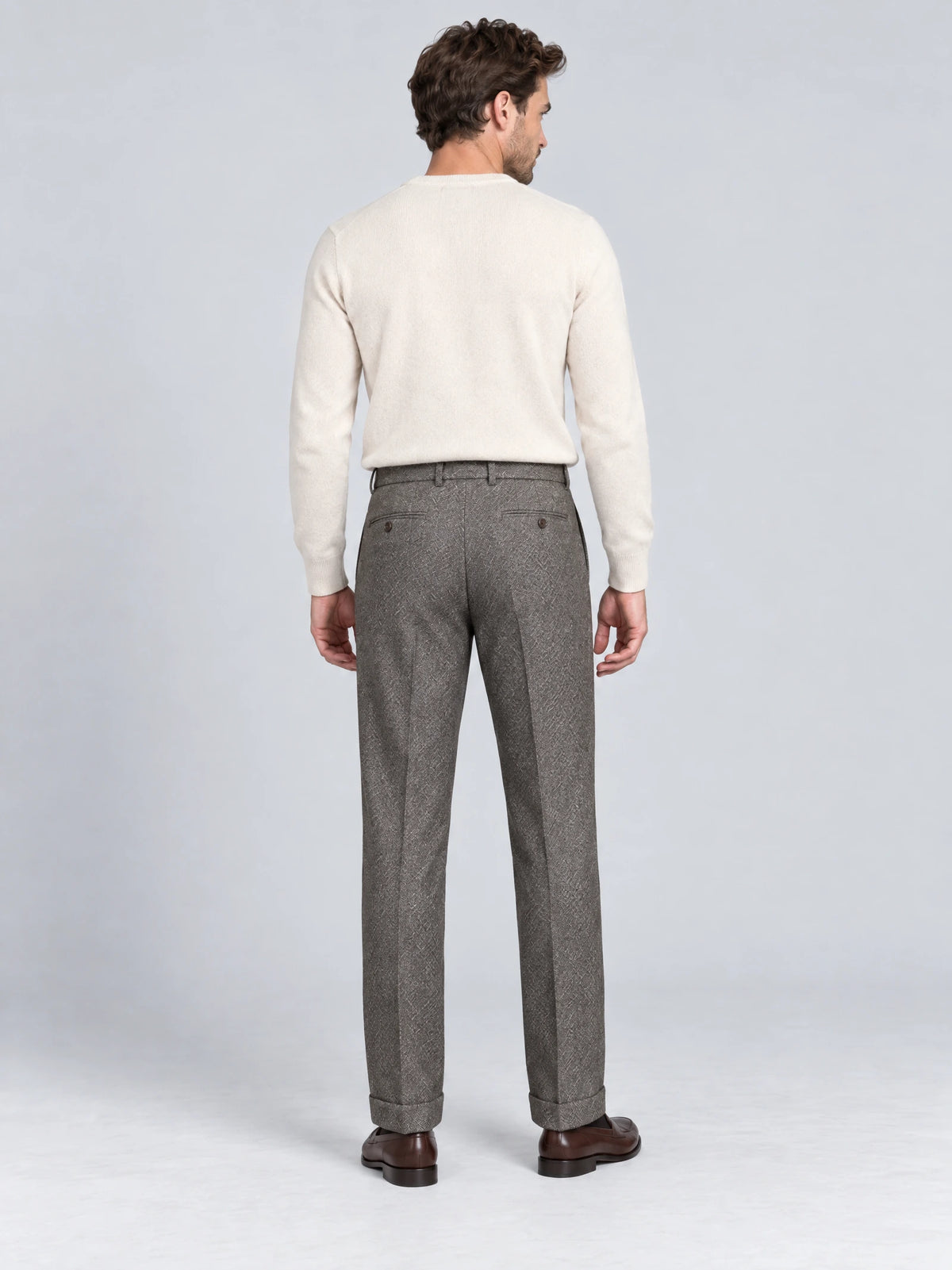Rear studio view of a model wearing Gray woolen herringbone formal pants with buttoned back pockets and cuffed hems.