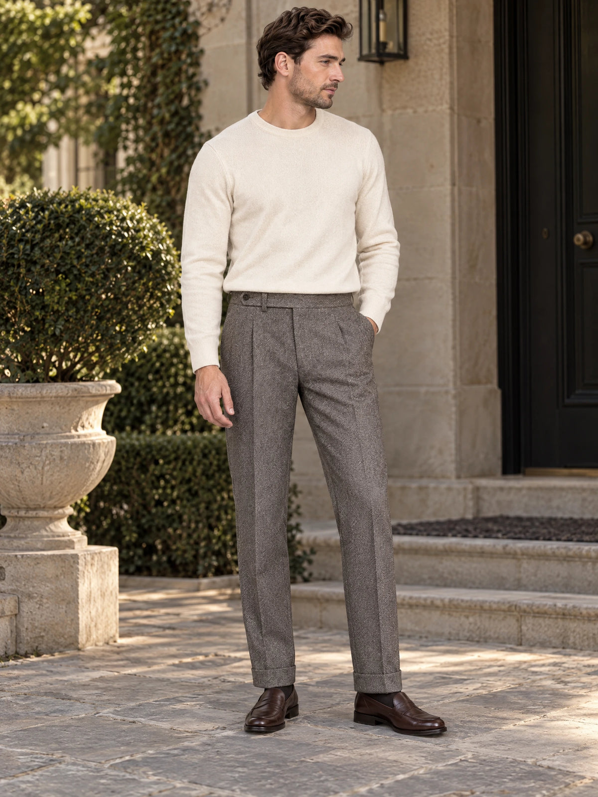 Model wearing Gray woolen herringbone formal pants with a white sweater outside a stone-fronted building.