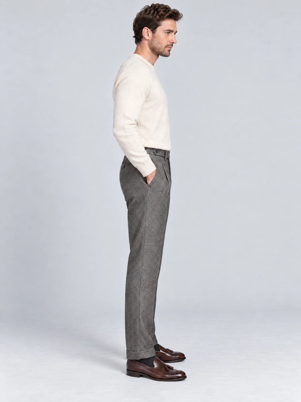 Side studio view of a model wearing Gray woolen herringbone pattern formal pants with a high waistband and side pocket.