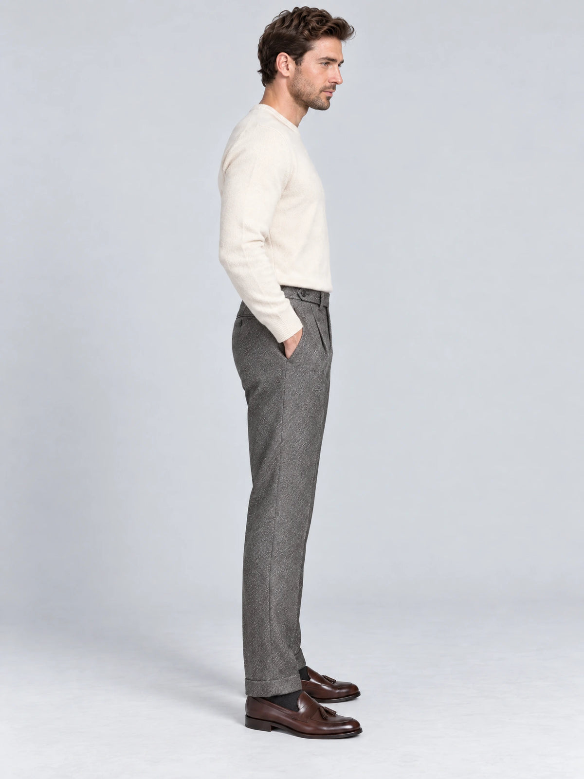 Side studio view of a model wearing Gray woolen herringbone pattern formal pants with a high waistband and side pocket.