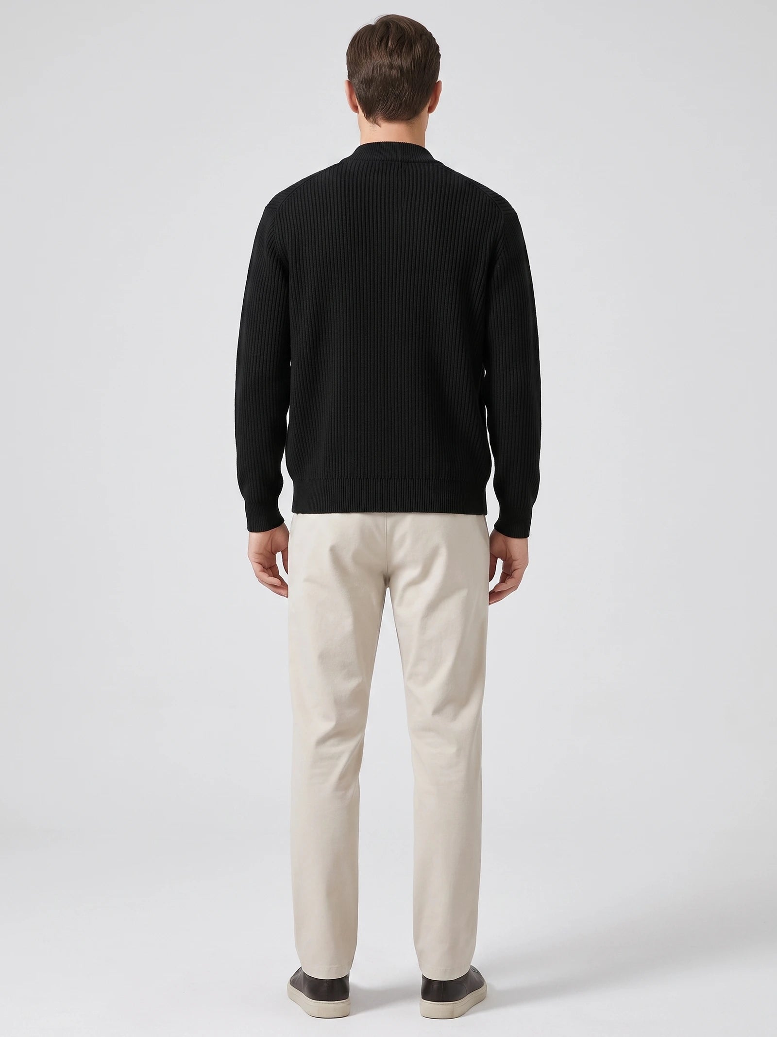 Rear studio view of a model wearing a Black zip up cardigan with vertical ribbed knit texture and a stand collar.